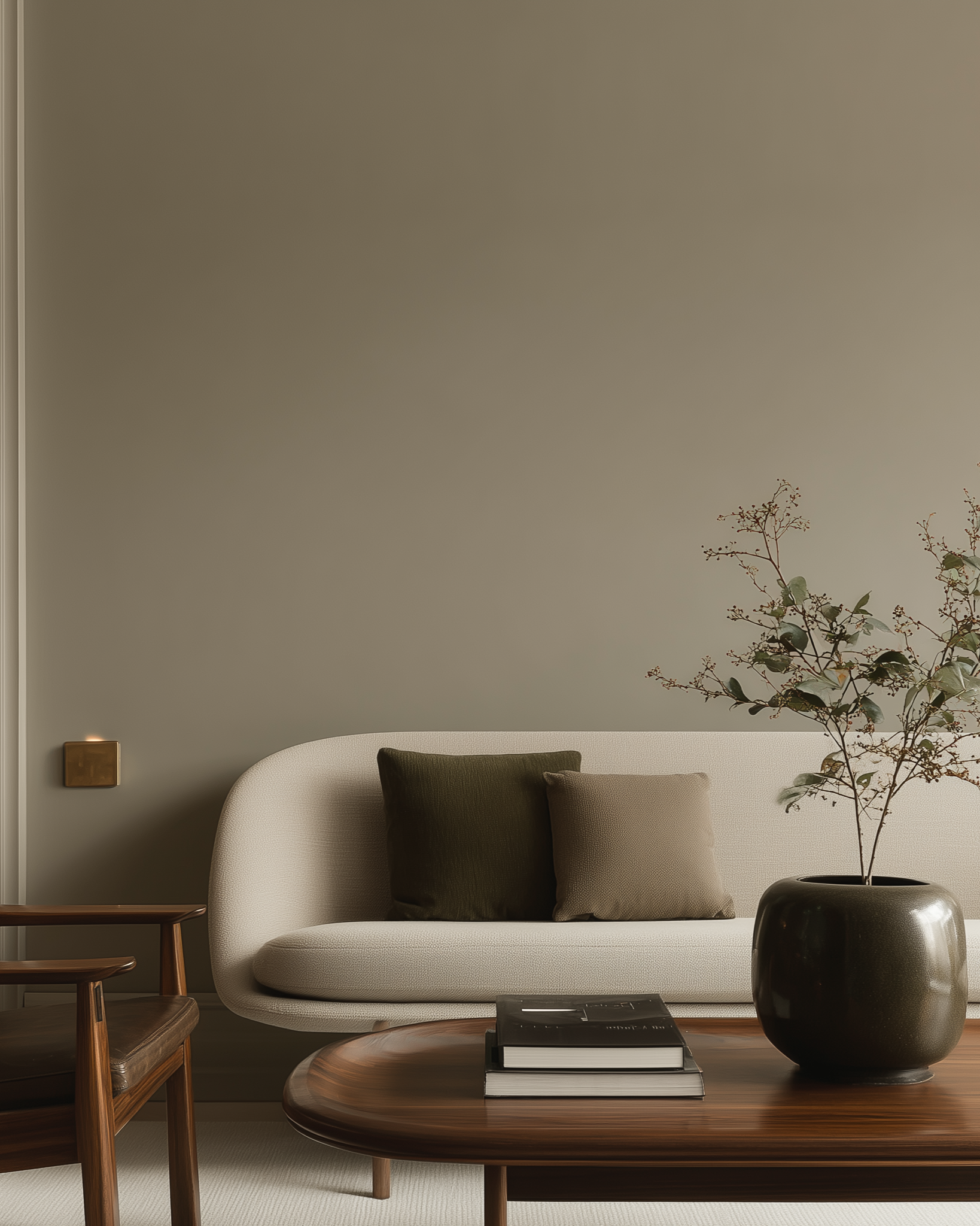 Minimalist living room with a cream-colored sofa, two cushions, a wooden coffee table with books, and a large dark vase with branches.