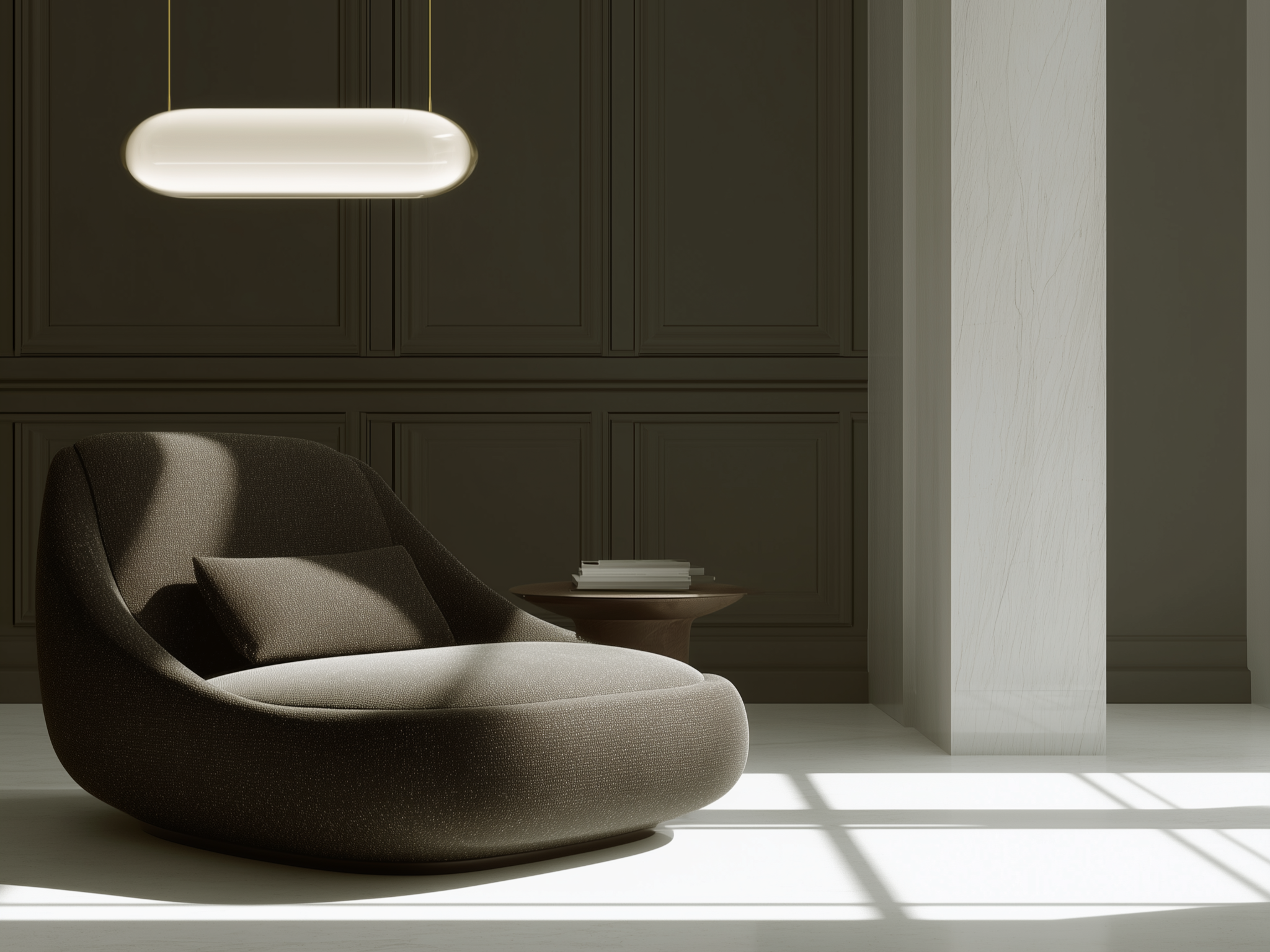Modern interior with a dark brown curved lounge chair with a matching pillow, gray paneled wall, small round wooden side table with books, white marble column, and sunlight casting shadow on white floor.