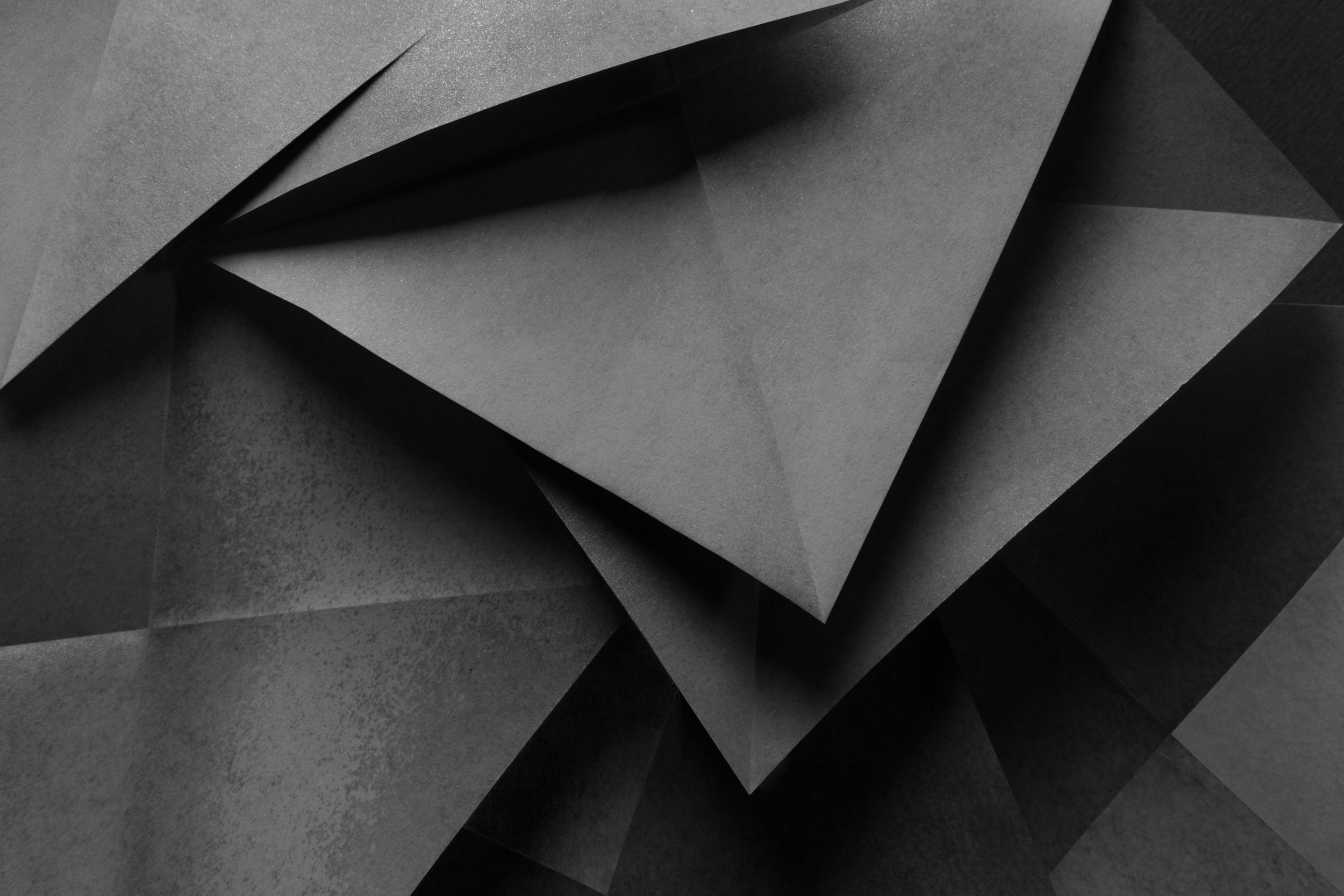 Abstract image of overlapping black and dark gray paper sheets with various textures and shadows.