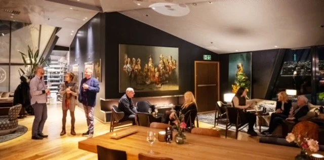 Innendørs restaurant eller kafé med mennesker som spiser og snakker, dekorert med kunst på veggene og planter.