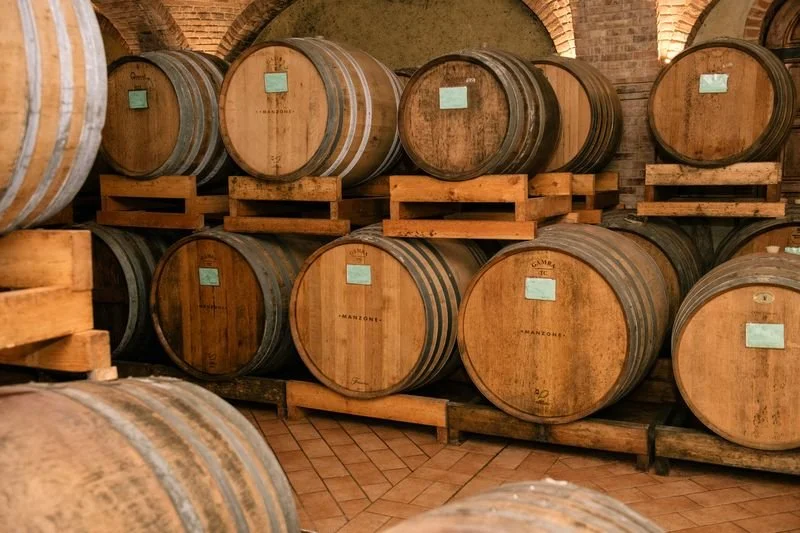 Rows of wooden wine barrels stored on wooden racks in a cellar with a brick ceiling.
