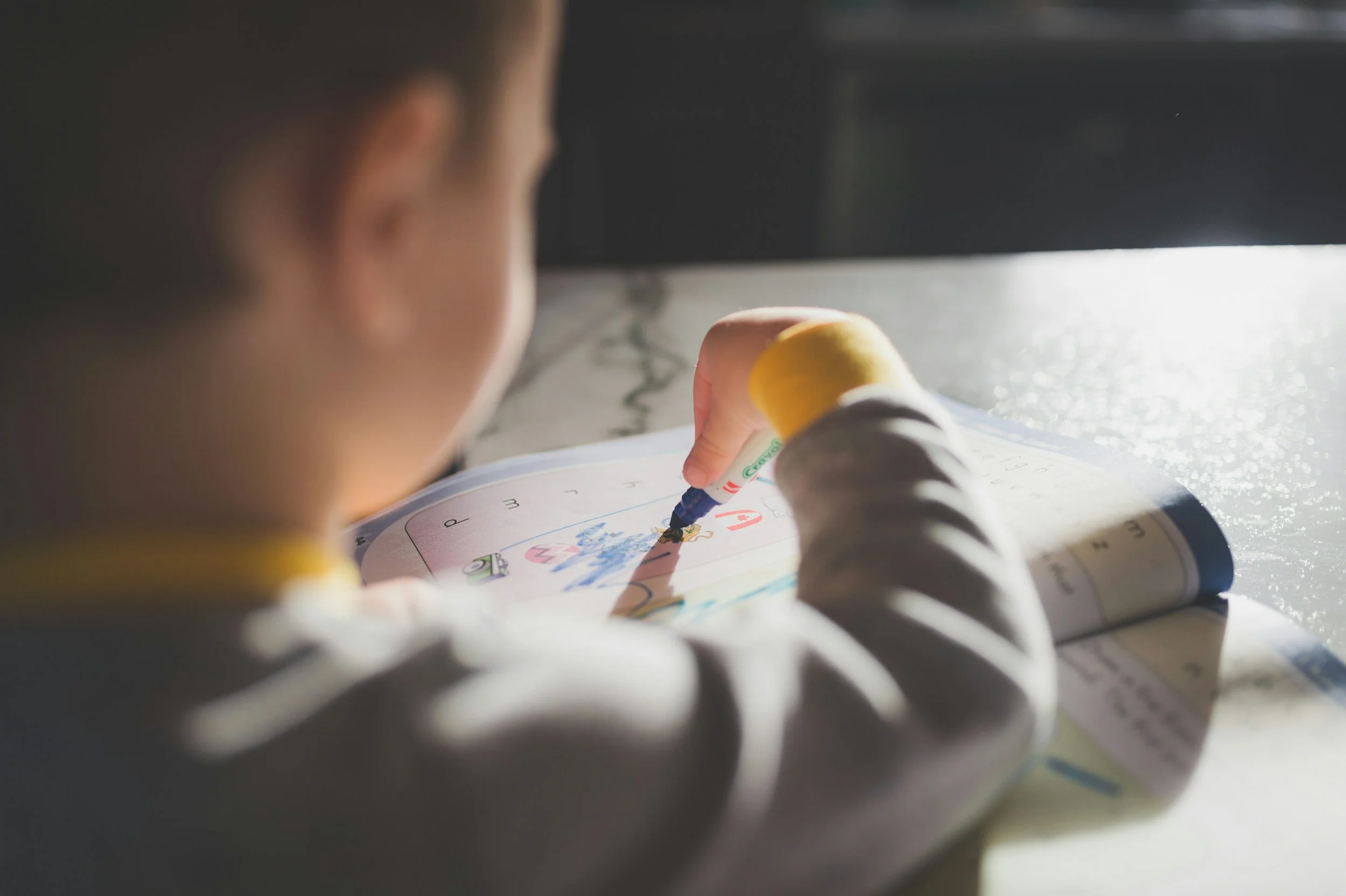 A young child sitting at a table, coloring in a children's book with a marker.