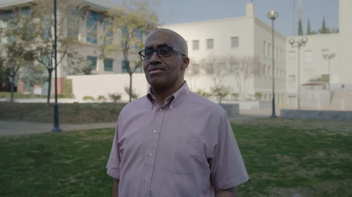Black man, pensive, standing on a field in front of a government building