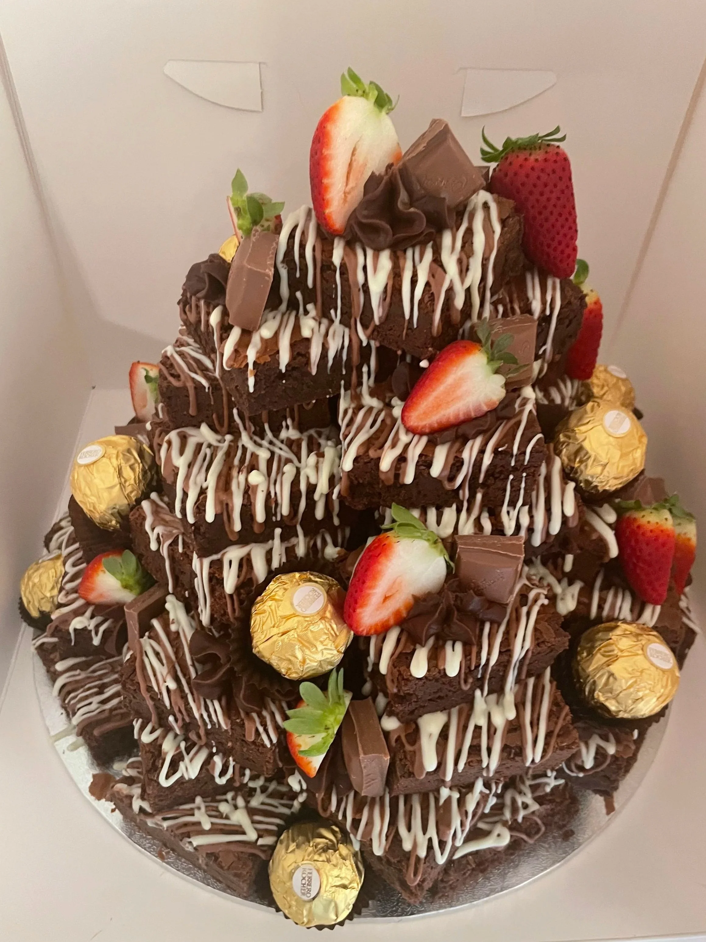 Chocolate brownie tower decorated with strawberries, chocolate pieces, white and dark chocolate drizzle, and Ferrero Rocher chocolates.