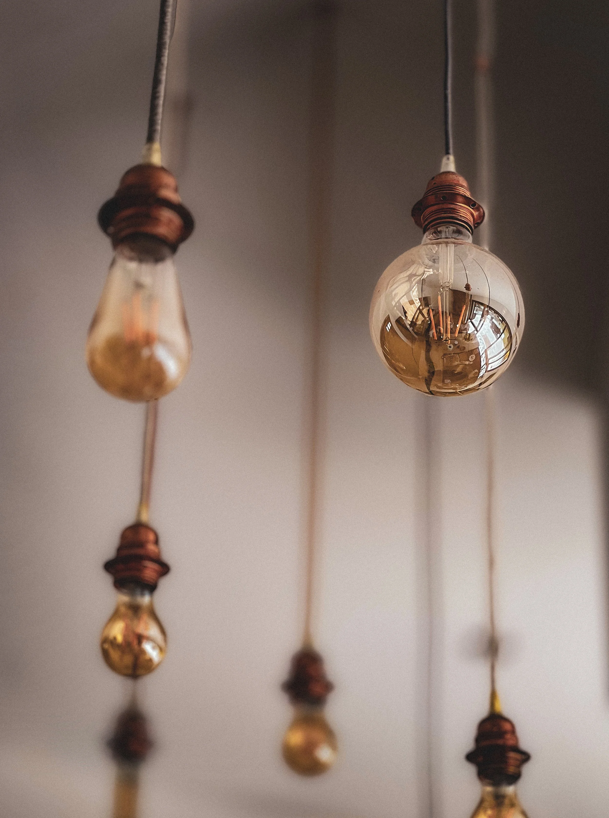 Ampoules électriques suspendues au plafond, dont une est une ampoule en verre transparent, les autres étant des ampoules en forme de goutte avec une couleur dorée.