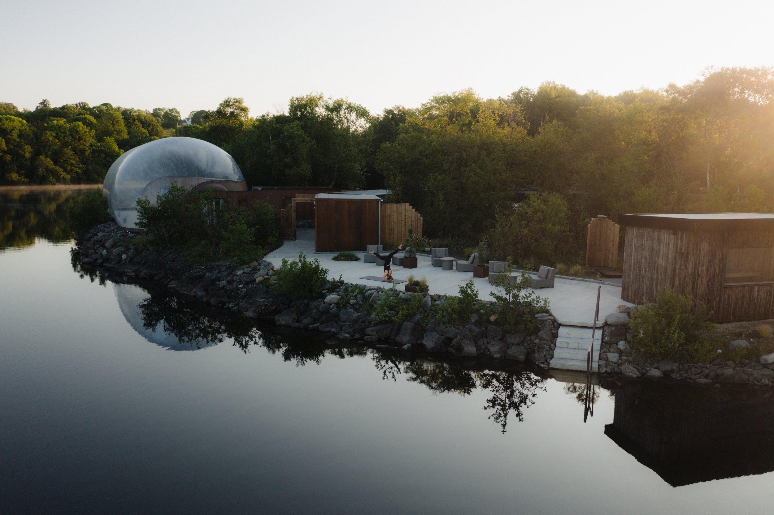 Casa moderna junto a un río, con paredes de madera y un domo transparente, rodeada de árboles.