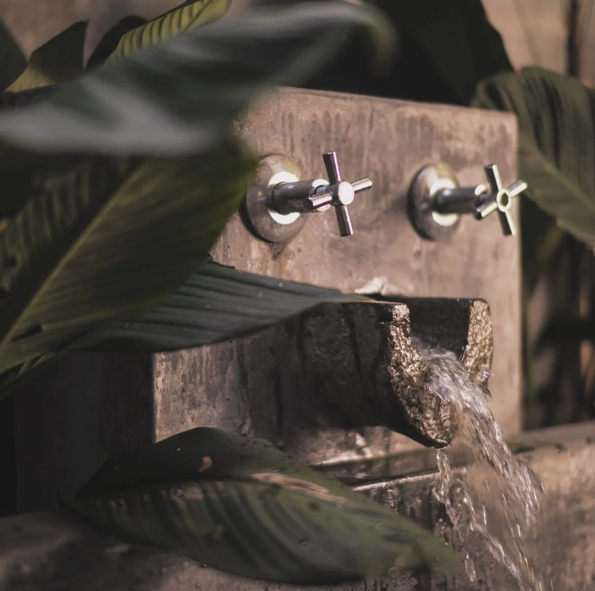 Sunset over the ocean at the beach with waves crashing on the shore and a few people in the water.