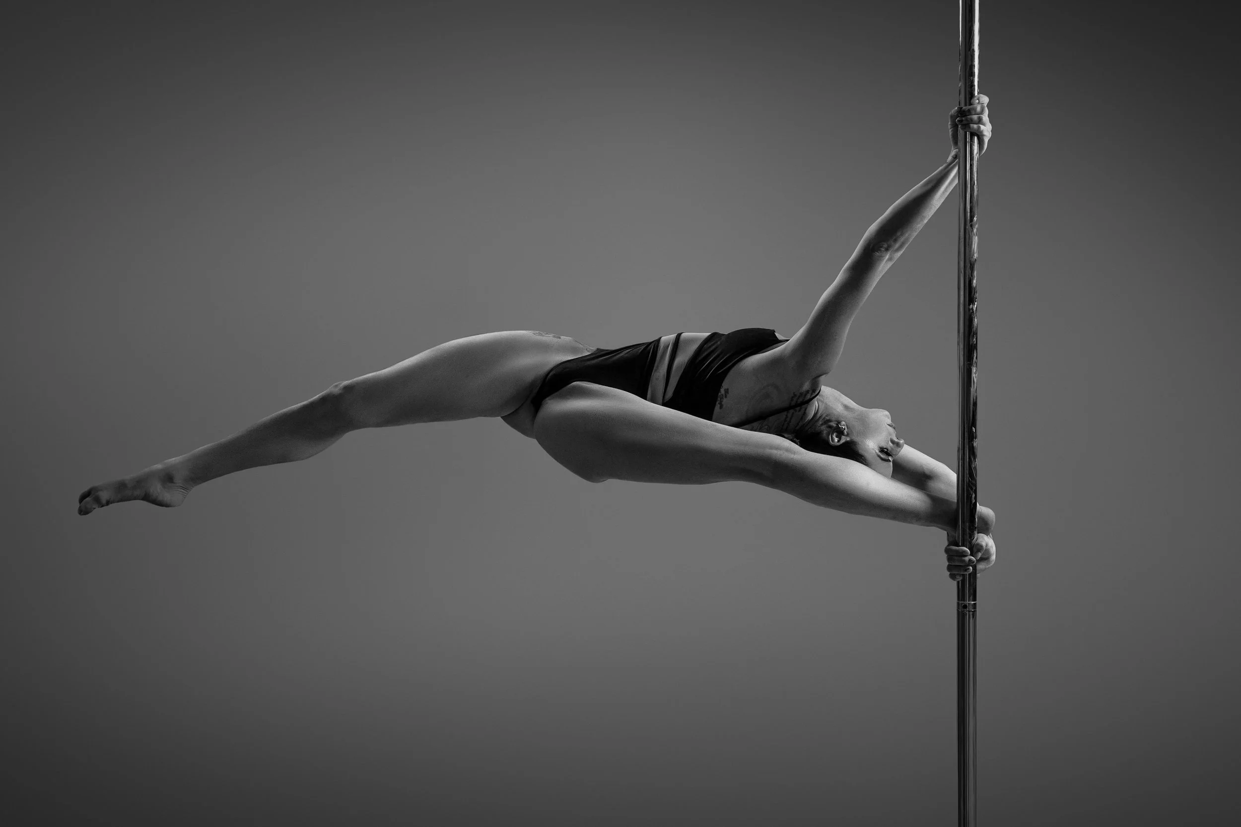 A woman performing an aerial pole dance on an outdoor rooftop at dusk, with a city skyline in the background.