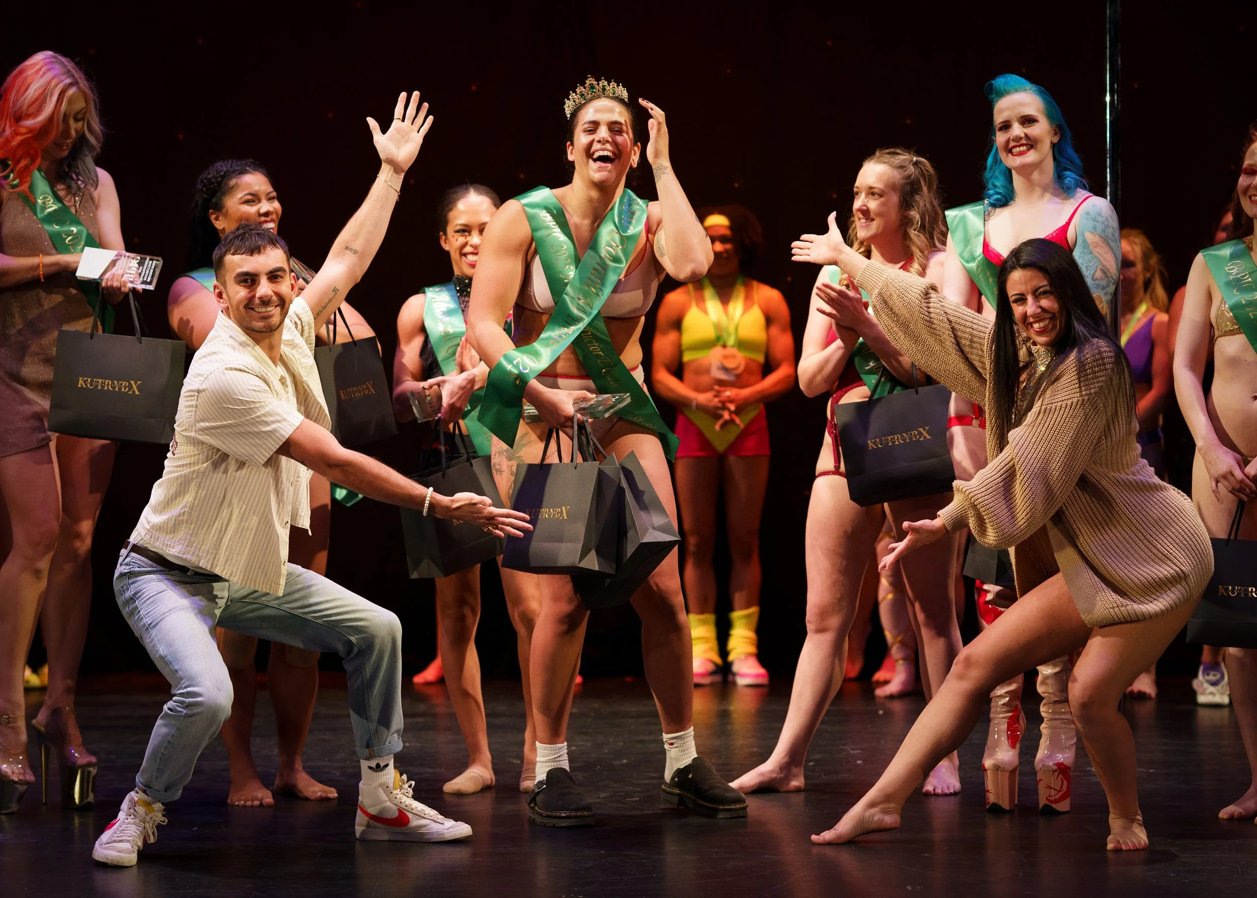 Dance studio with wooden floor, wall mirror, and a large phoenix logo in orange on the wall, with several metal dance poles.
