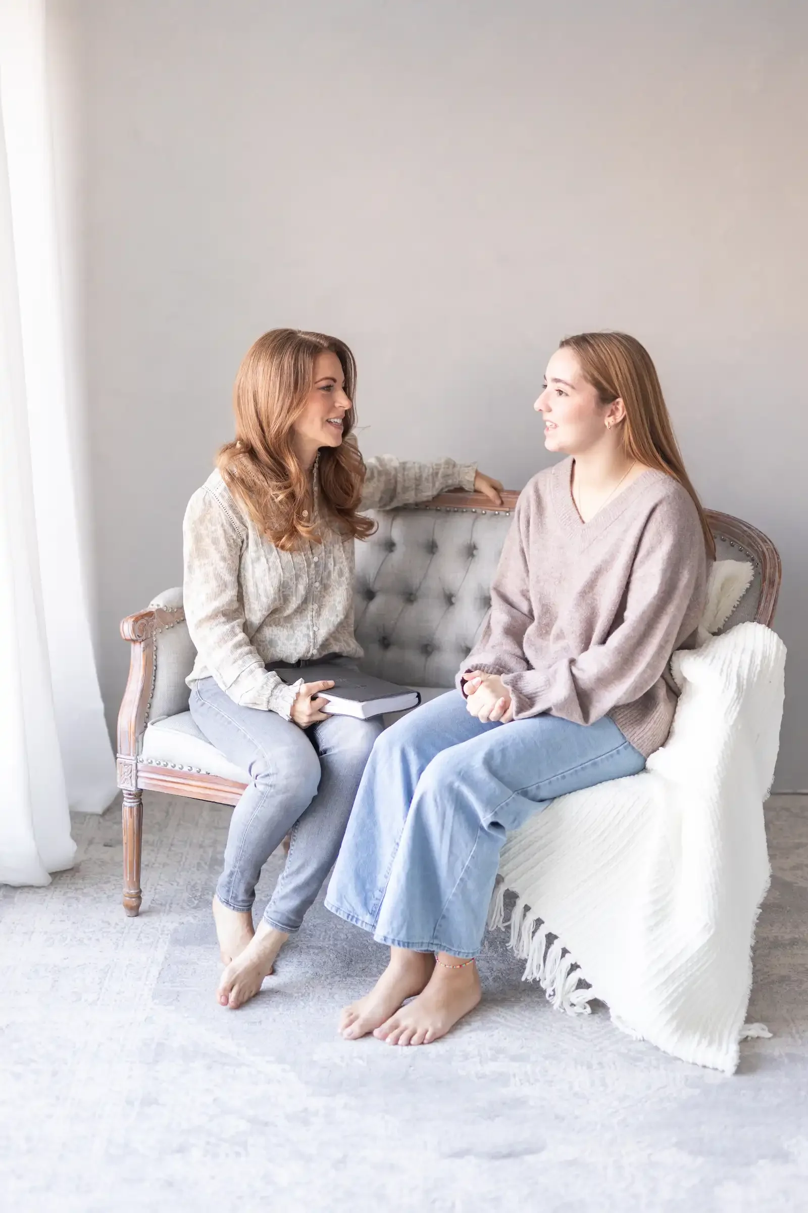 Two women sitting on a vintage sofa having a conversation indoors.