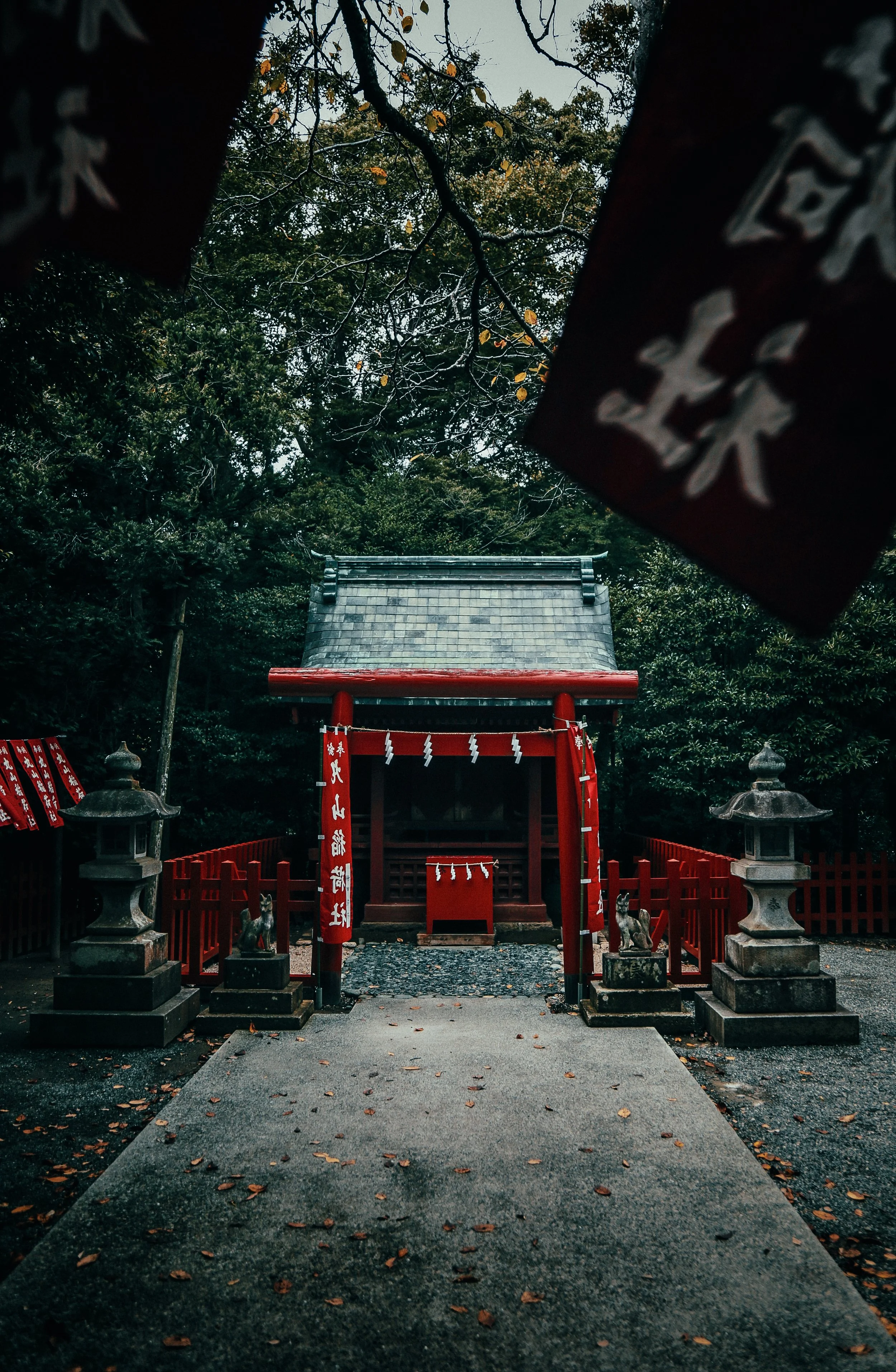 Een traditioneel Japans heiligdom genesteld in een bos, met een rode torii-poort, stenen lantaarns en houten beelden, omgeven door groene bomen.