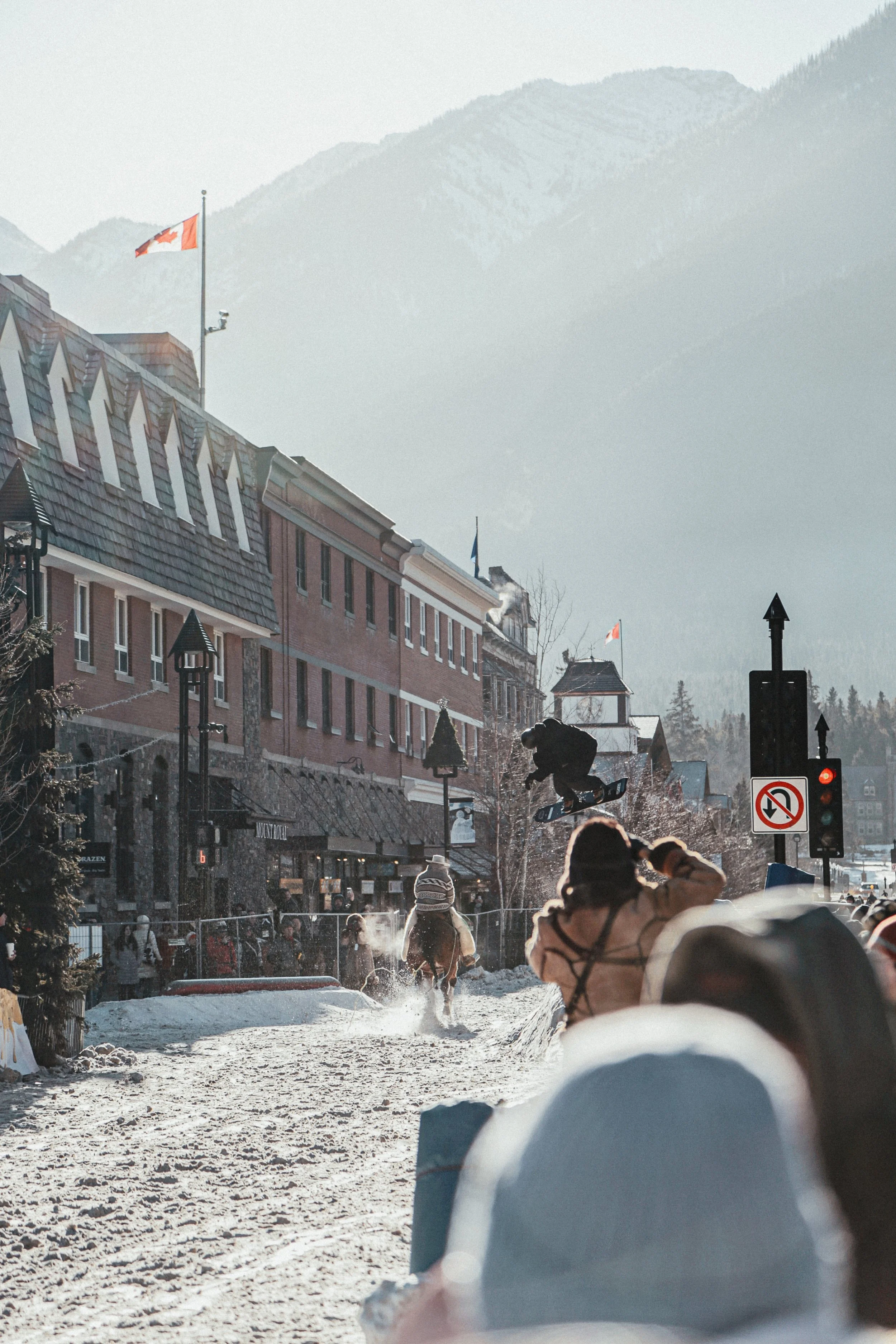 Sneeuwscene met skiërs en snowboarders in een bergdorp. Mensen dragen winterkleding onder een kleurrijke zon. Achter gebouwen en bergen.