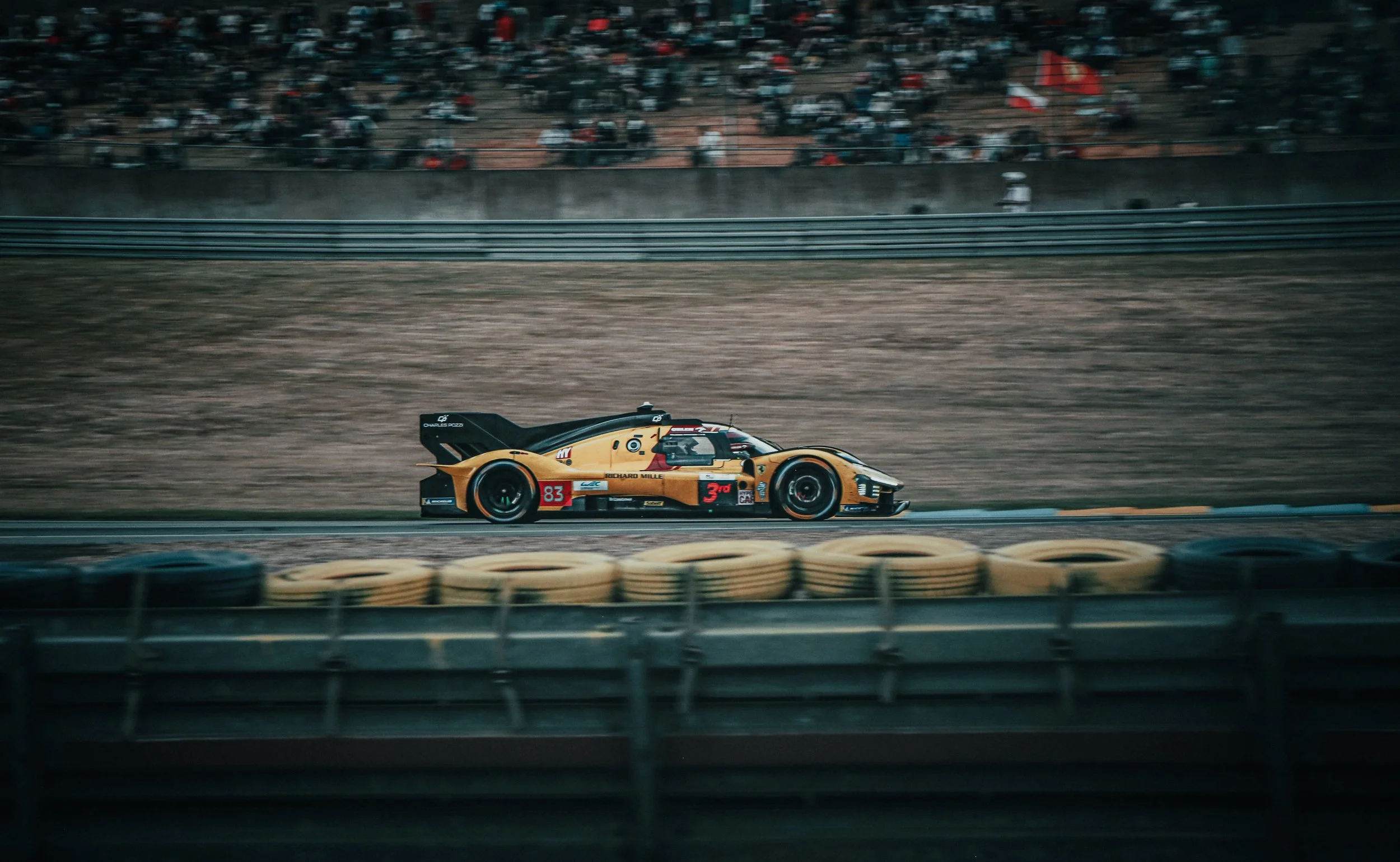 Een raceauto rijdt op een circuit met tribunes vol toeschouwers.