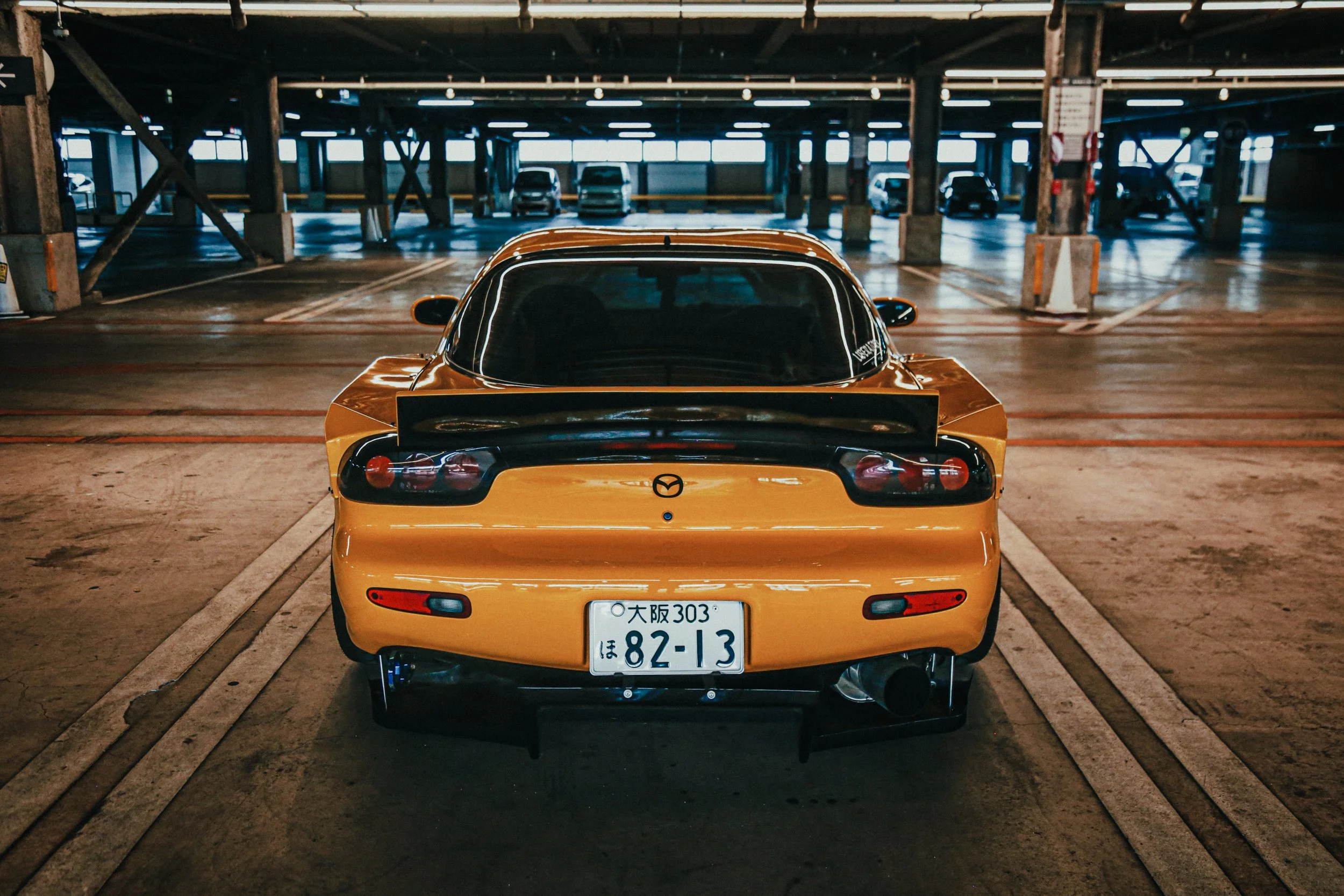 Geel sportauto geparkeerd in een parkeergarage met meerdere auto's op de achtergrond.