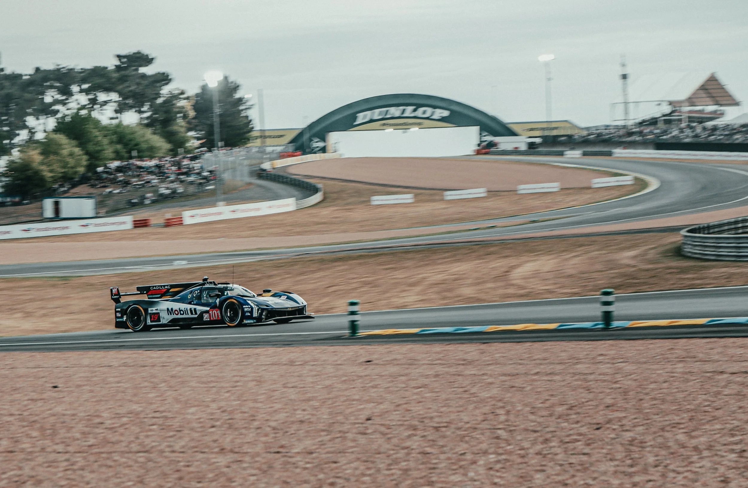 Een raceauto rijdt op een circuit met een Dunlop-boog in de achtergrond.