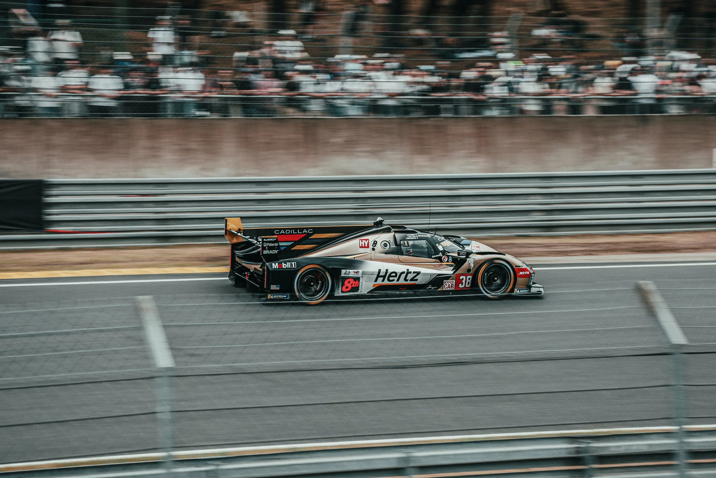 Raceauto op een circuit tijdens een race met publiek op de achtergrond.