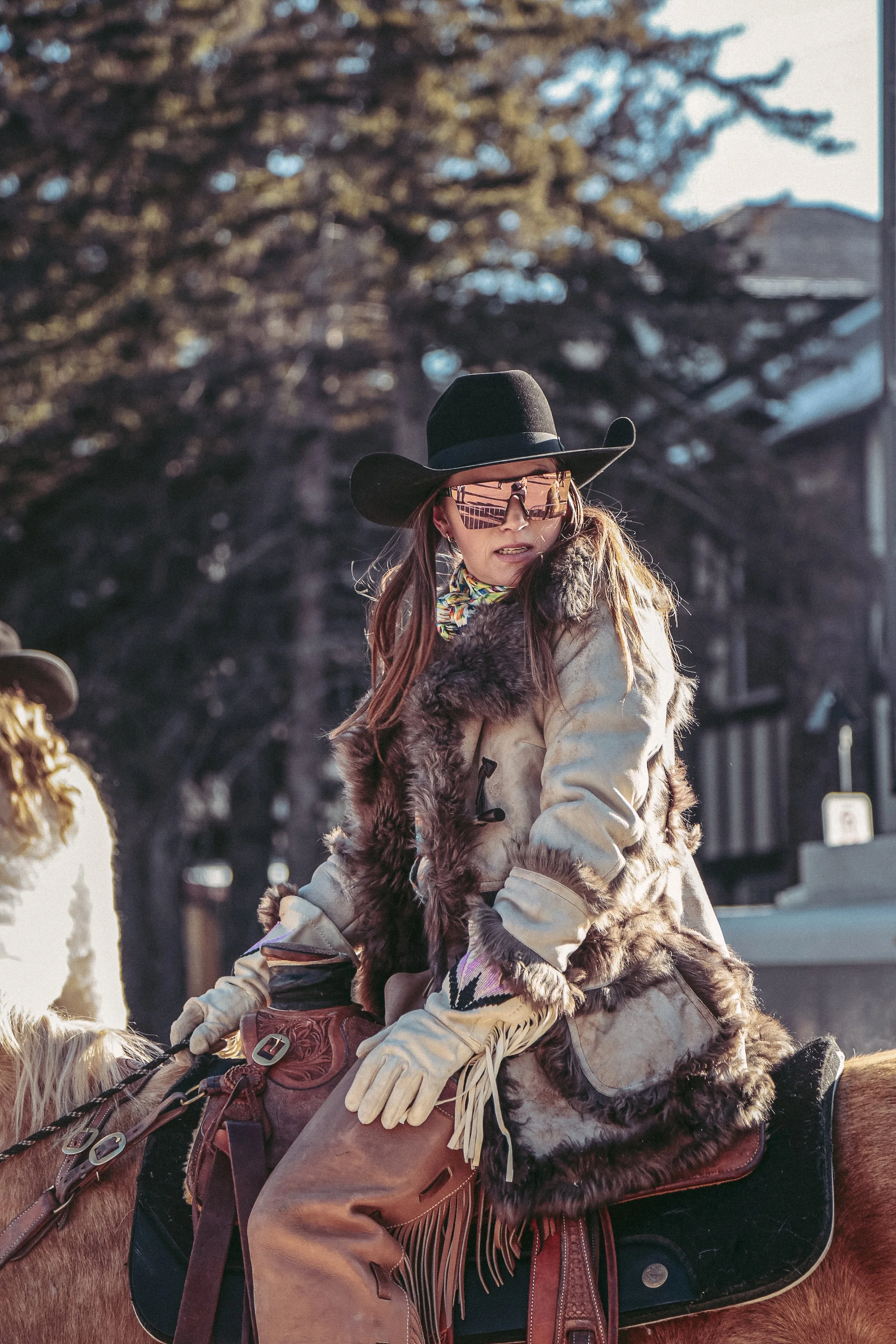 Vrouw met breedhoed, grote zonnebril en bontjasje rijdt op een paard.