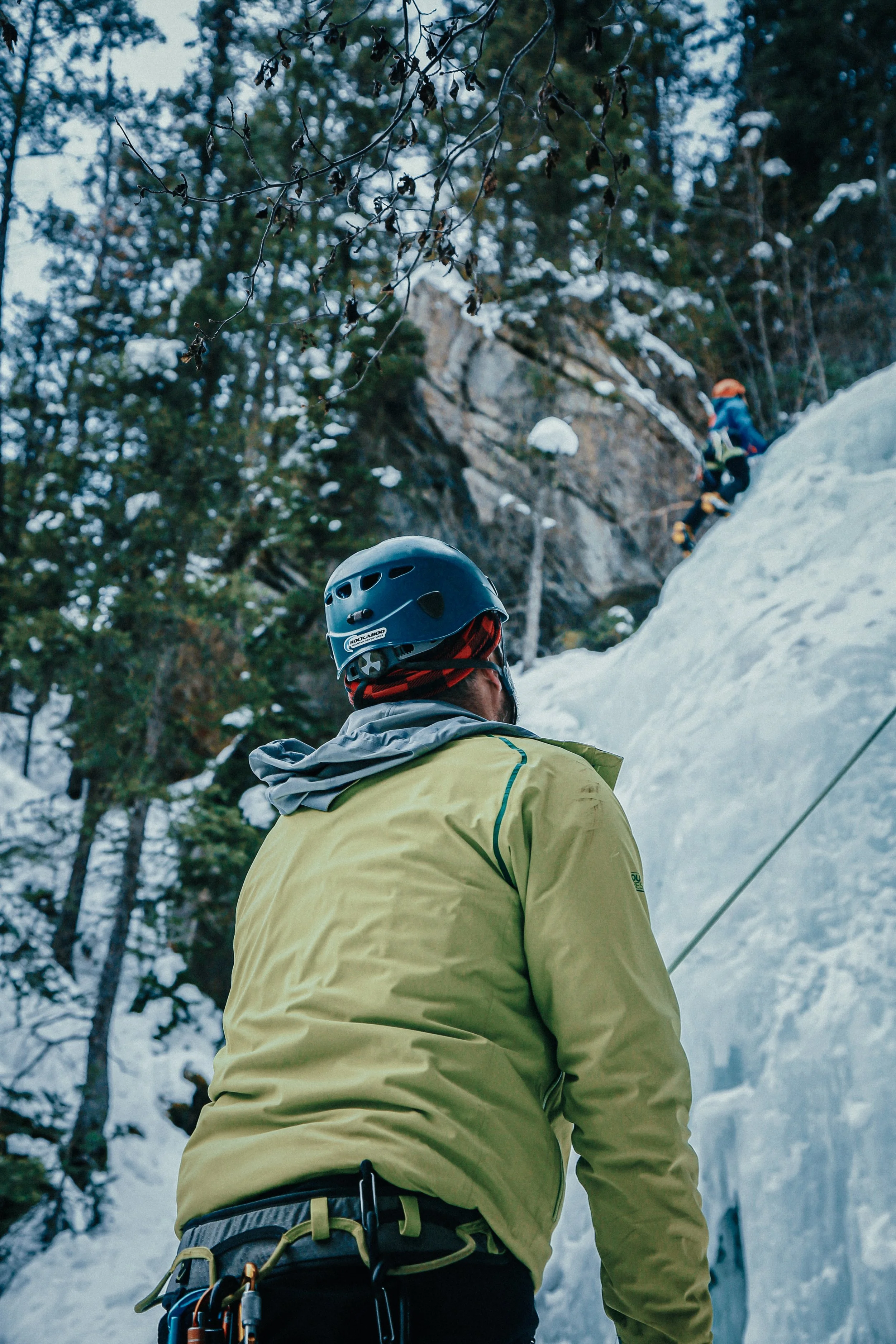 Een man met helm en klimuitrusting kijkt naar een ijswand tijdens het klimmen in de bergen.