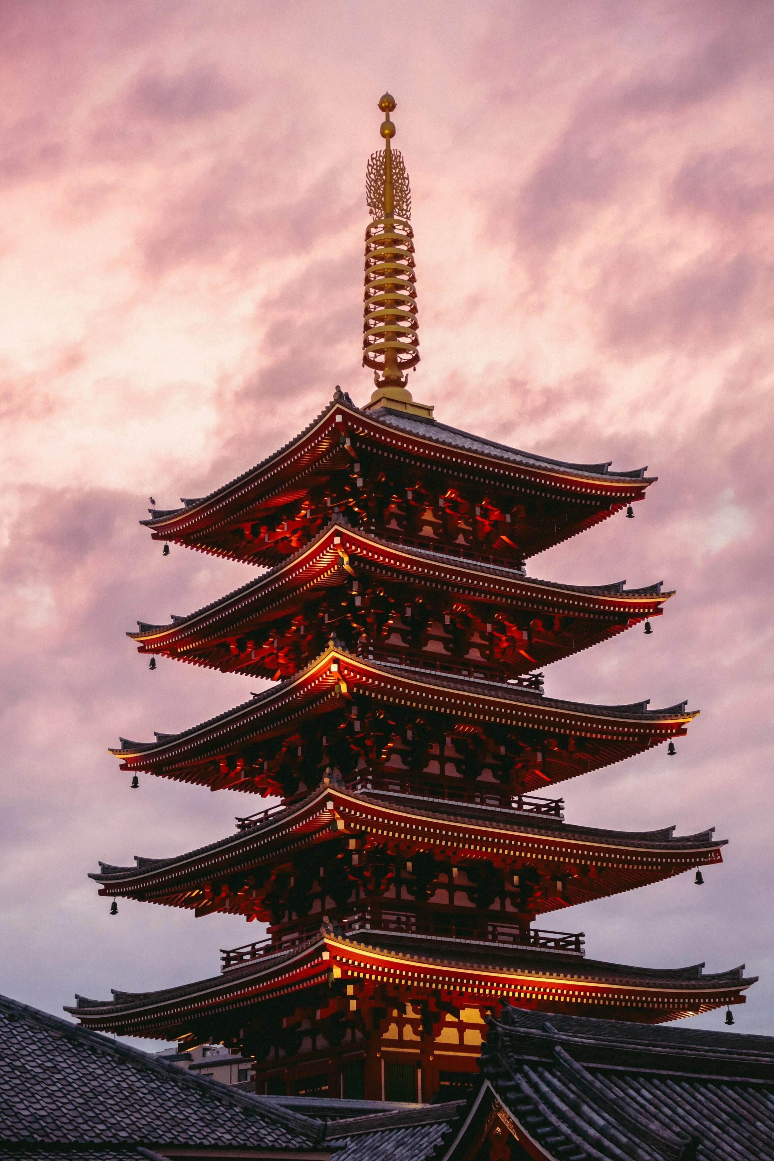 Een traditionele Japanse pagode met meerdere verdiepingen, verlicht tegen een roze hemel met wolken.