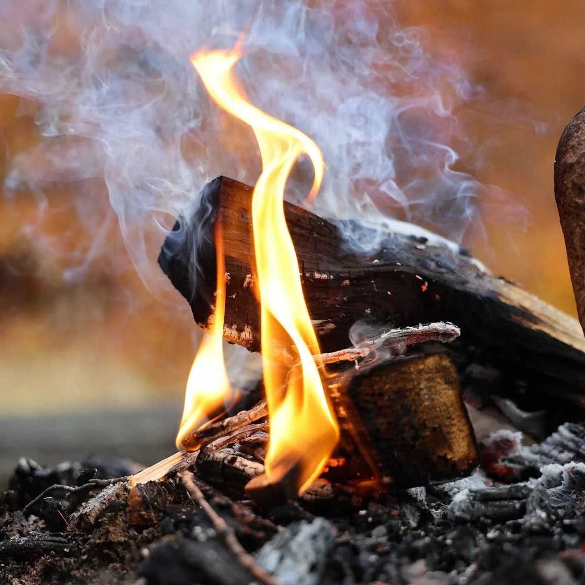 Billede af ild, der brænder på jord, med synlige flammer og røg.