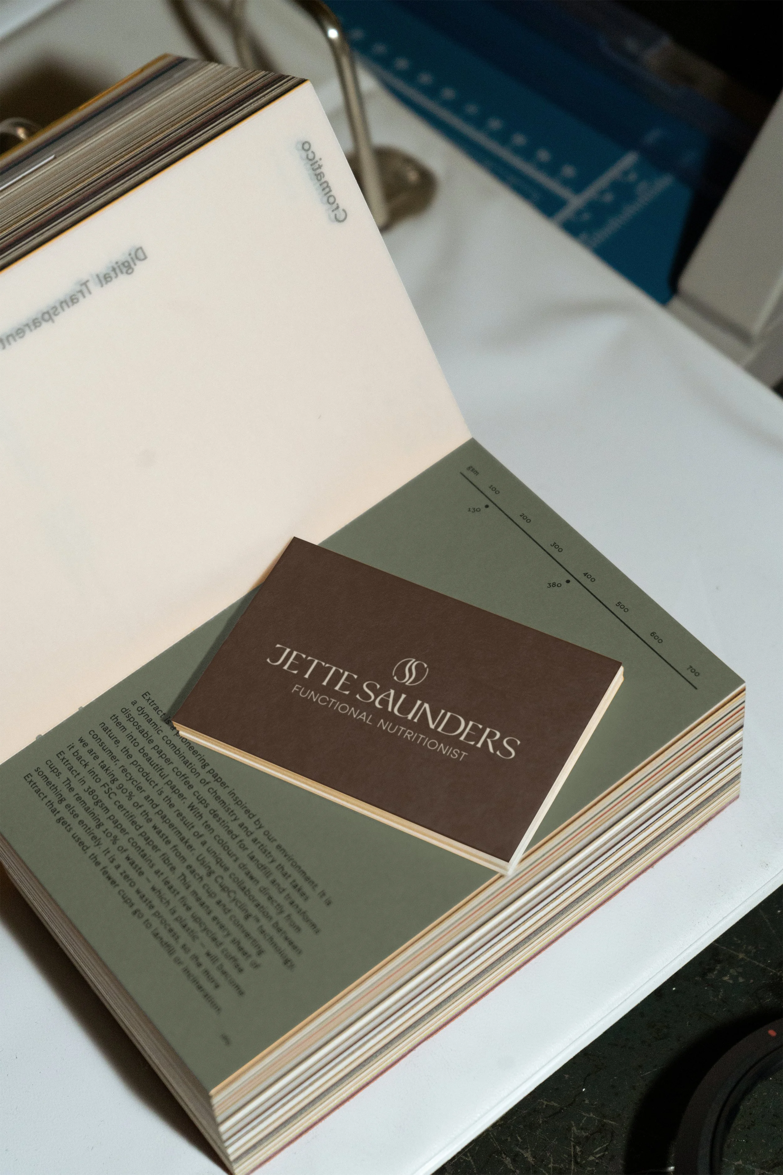 A booklet titled 'Jette Saunders Functional Nutritionist' resting on a larger open book or magazine on a white surface. The larger book has a green page with a measurement chart on it.