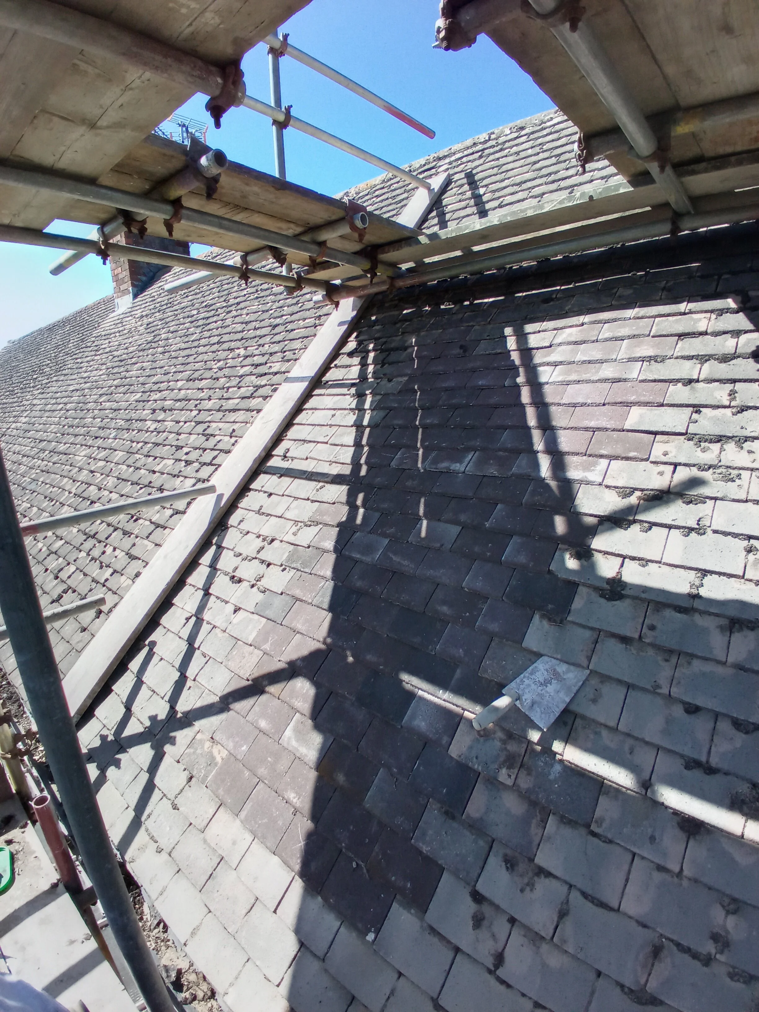 Construction scaffolding on a roof with shadow cast on tiles, under a clear blue sky.