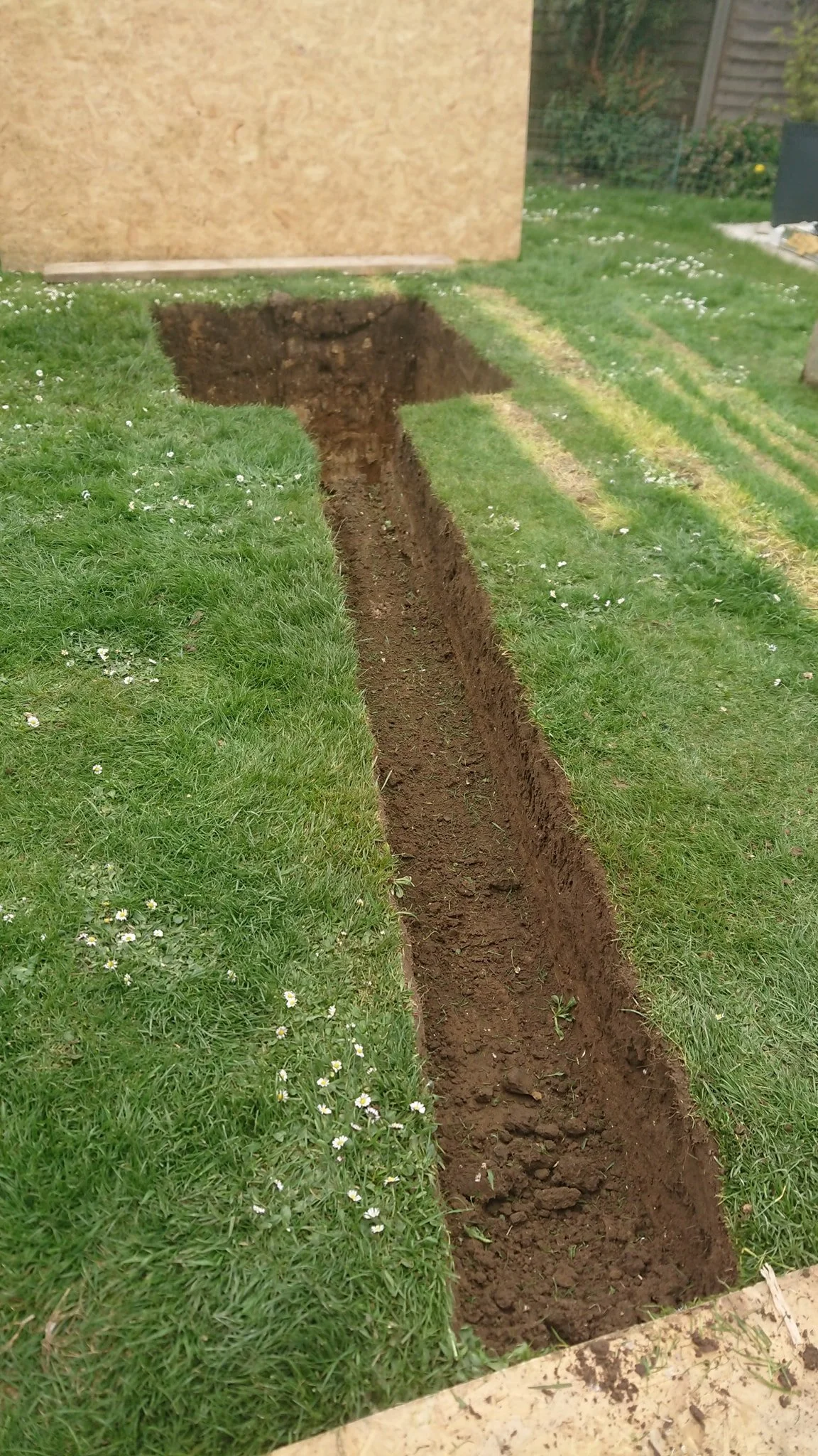 A freshly dug narrow trench in a green lawn, Soakaway trench
