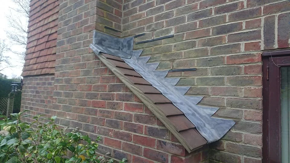 A brick house exterior with a partially installed metal roof flashing, extending from the chimney area to the edge of the roof.