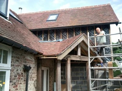A man working on the roof of a brick house under construction with scaffolding and roofing materials, during daytime.
