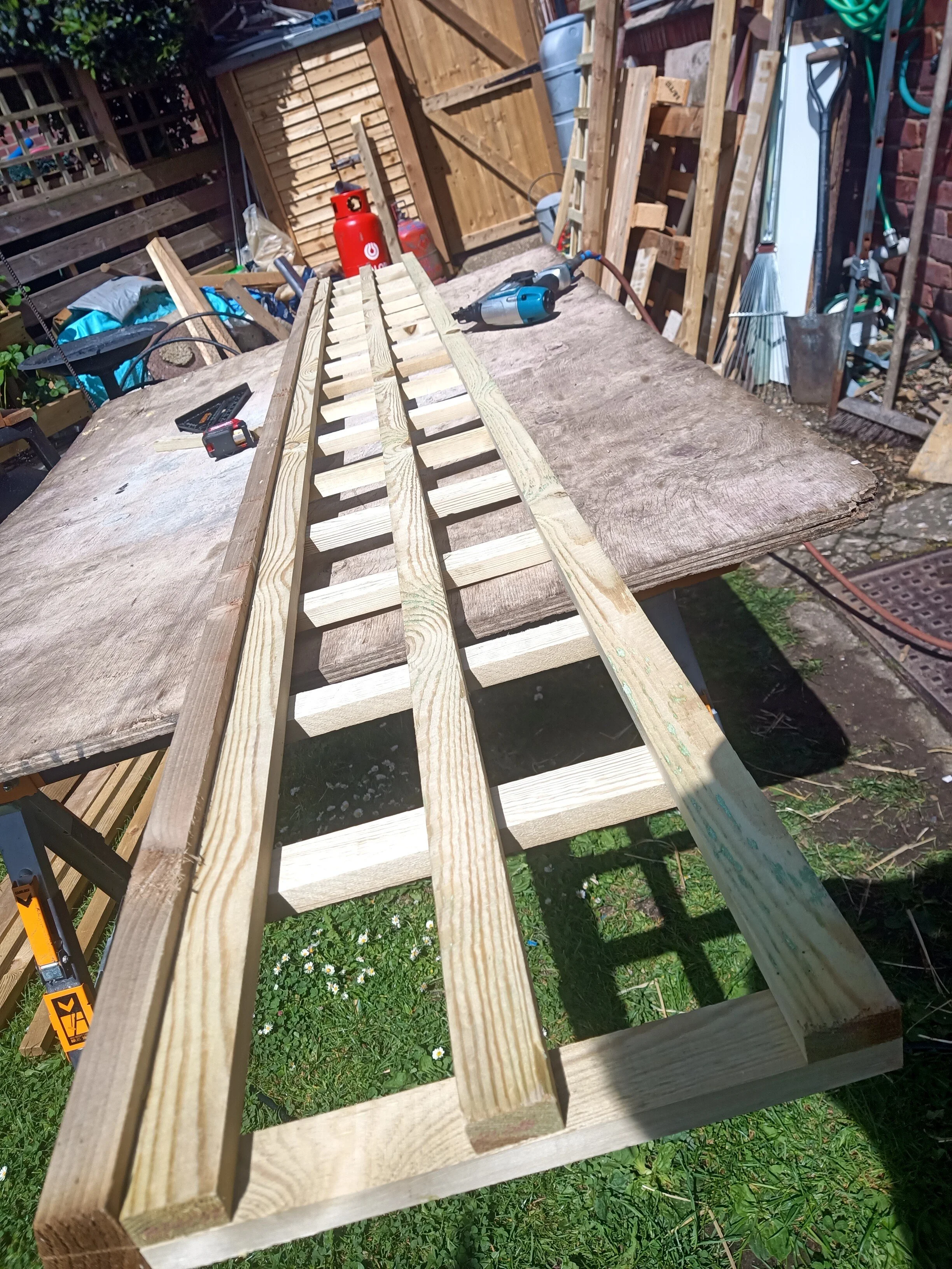 Wooden pallet frame being assembled outdoors on a wooden work table, with tools and materials around.