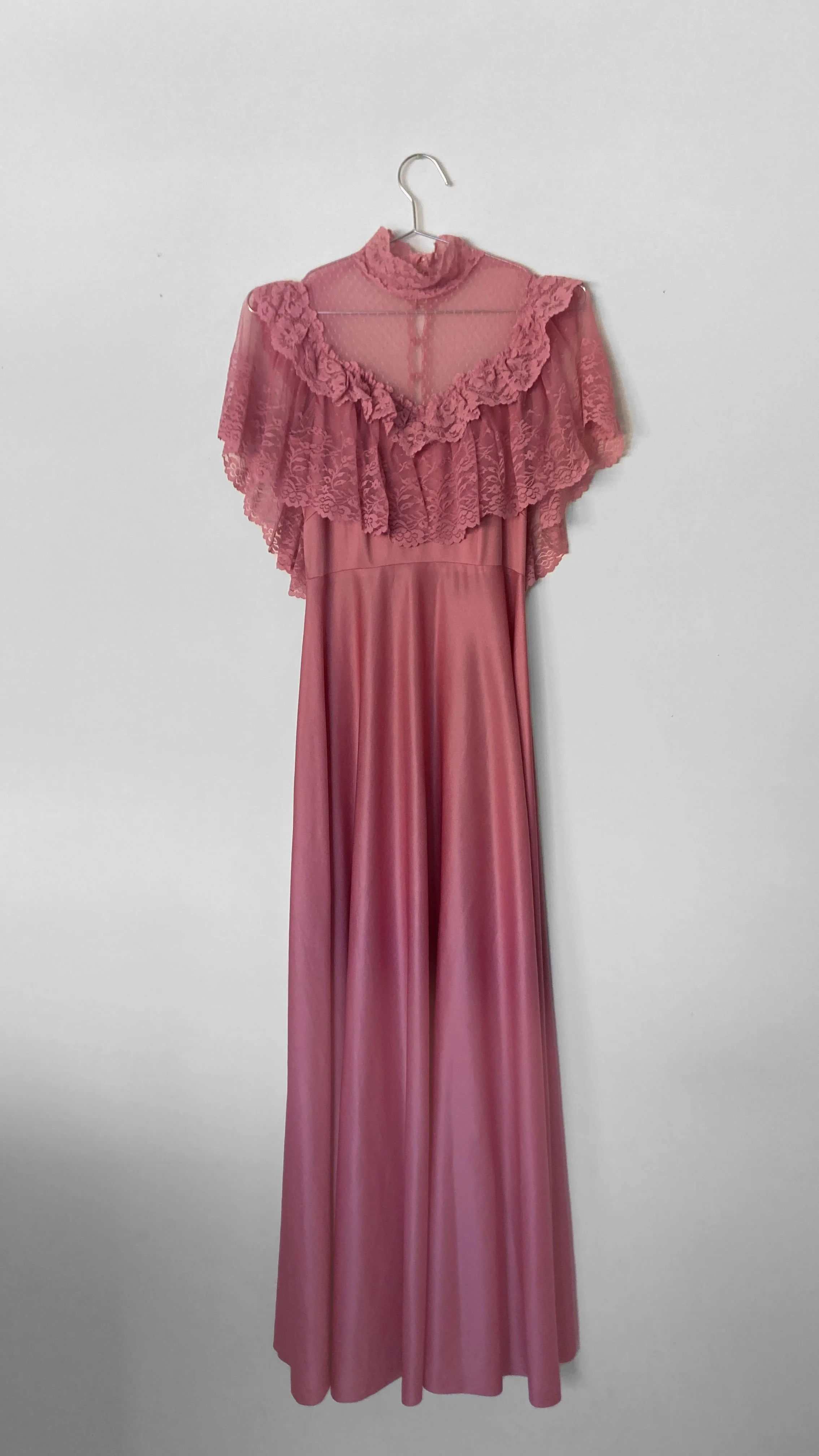 Full length view of the front of a rose pink floor length dress. The bodice is a sheer lace with ruffles and a lace high neck.