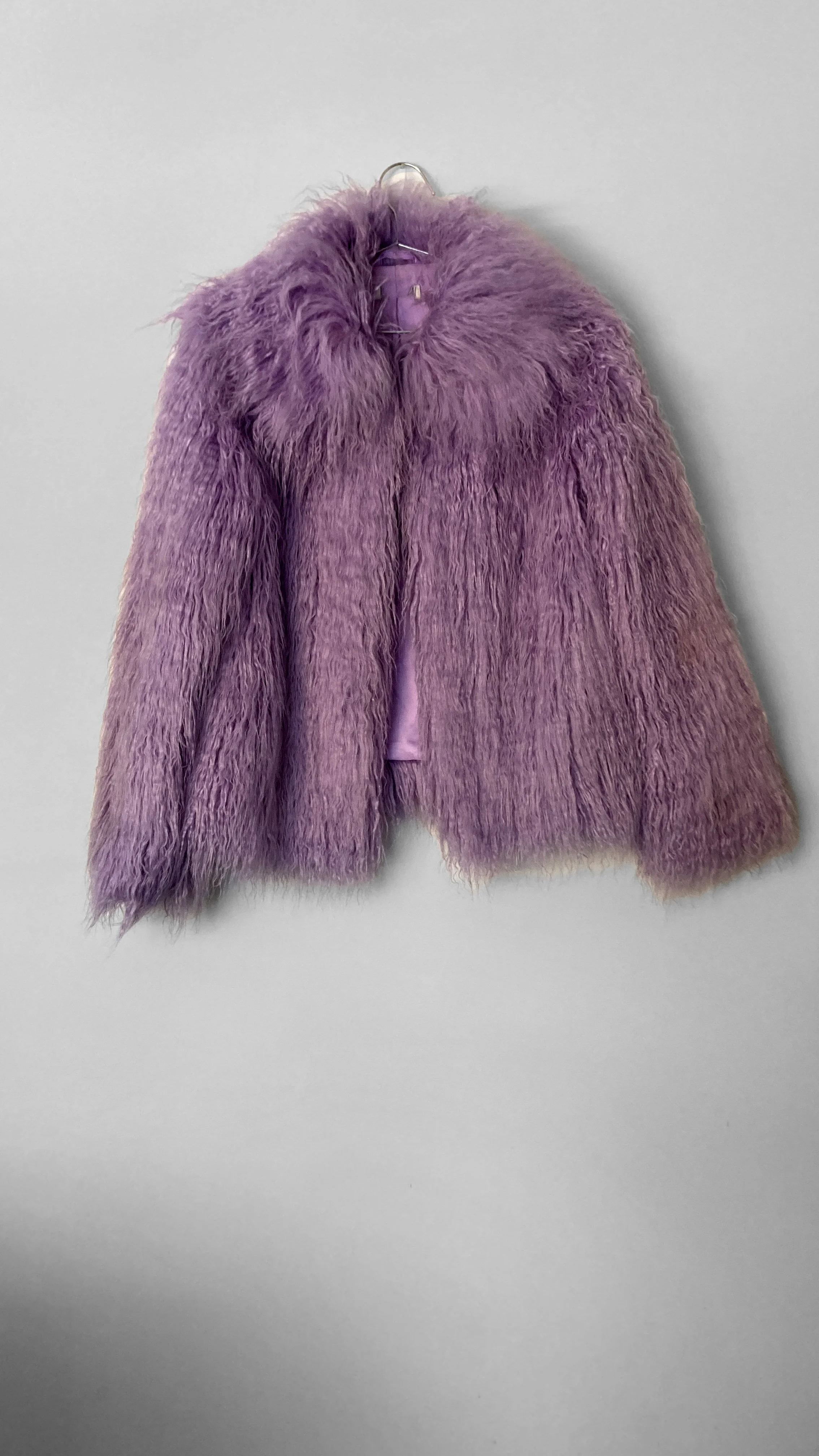 Full view of a lilac-purple hip length faux fur jacket. It has an oversized fur collar, and fastens down the centre front.