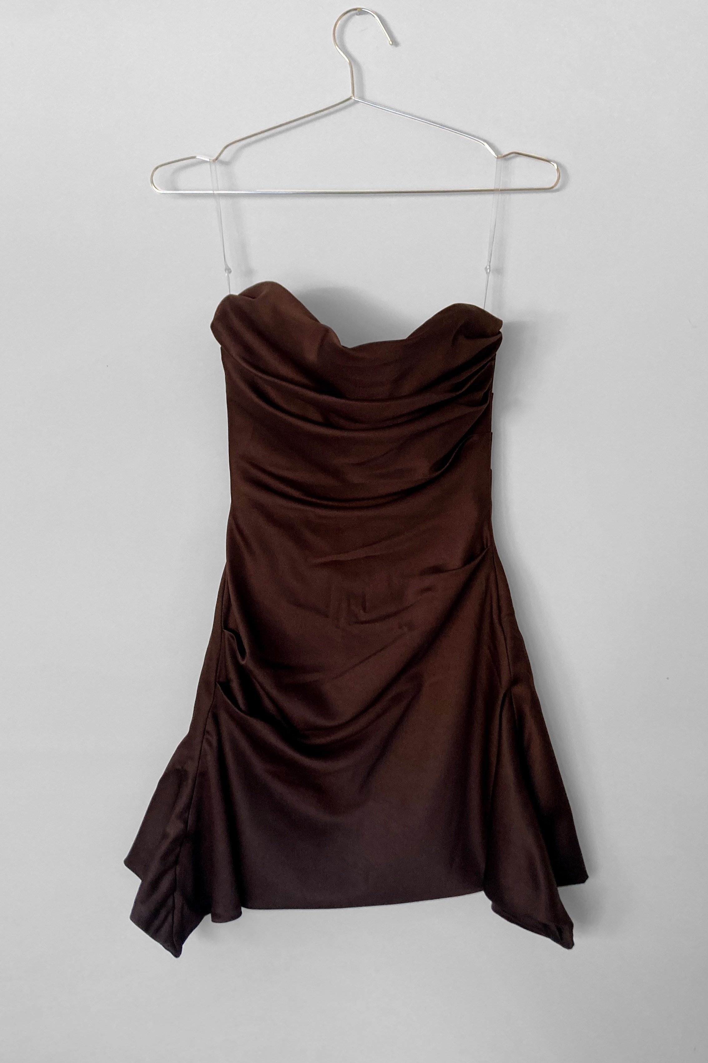 Full length view of a mini chocolate coloured cocktail dress, with soft draping over the bust, and the hem finishes longer at the sides, creating a waterfall effect.