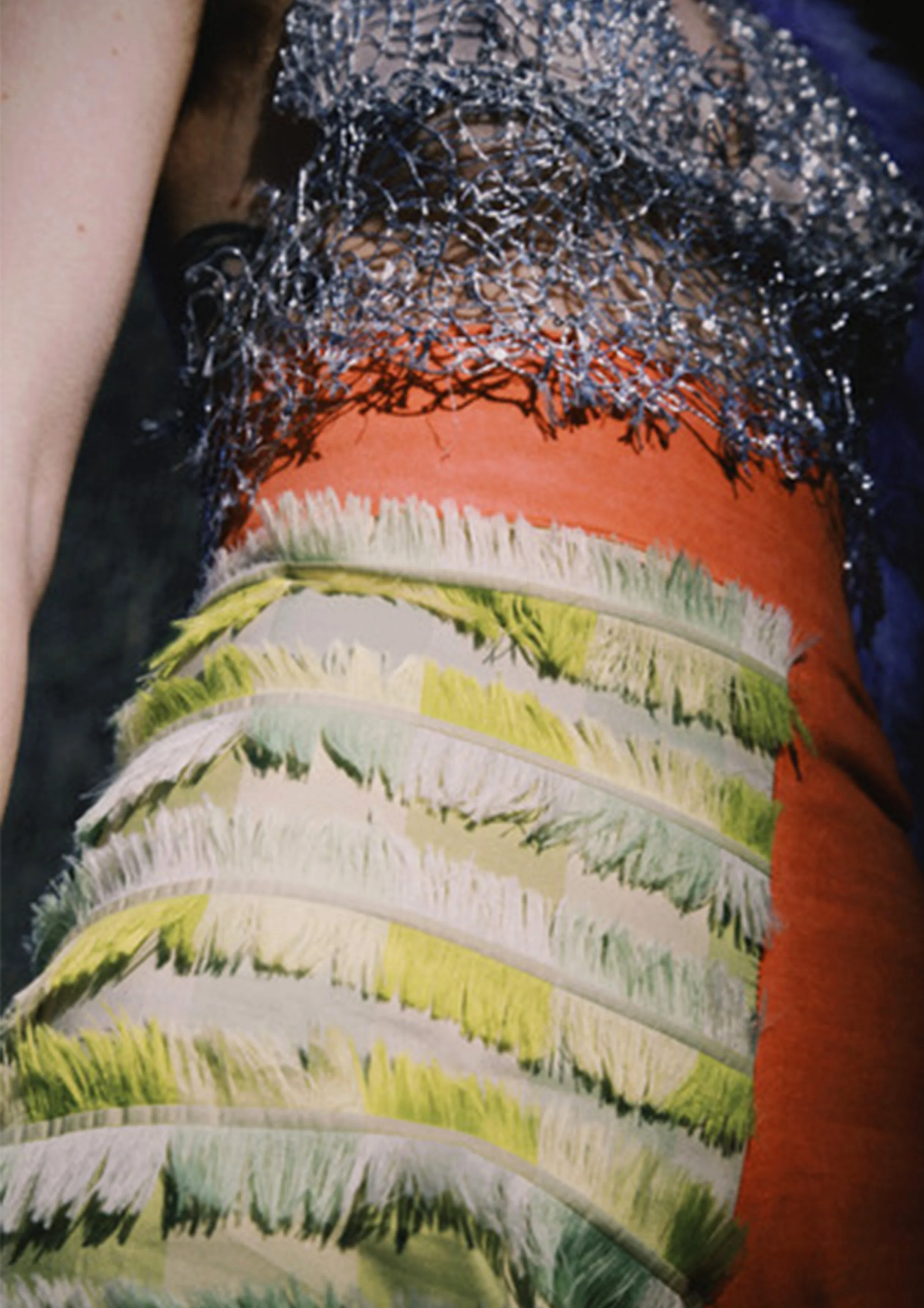 Close up image of a clown costume, featuring odd-legged trousers, one leg pink, the other green ruffled, and a silver web-like top.