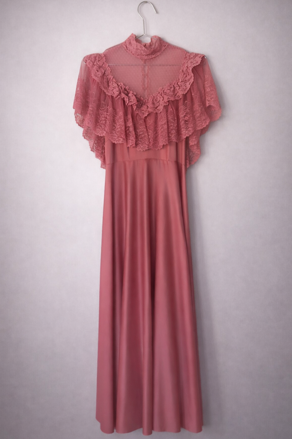 Full length view of the front of a rose pink floor length dress. The bodice is a sheer lace with ruffles and a lace high neck.