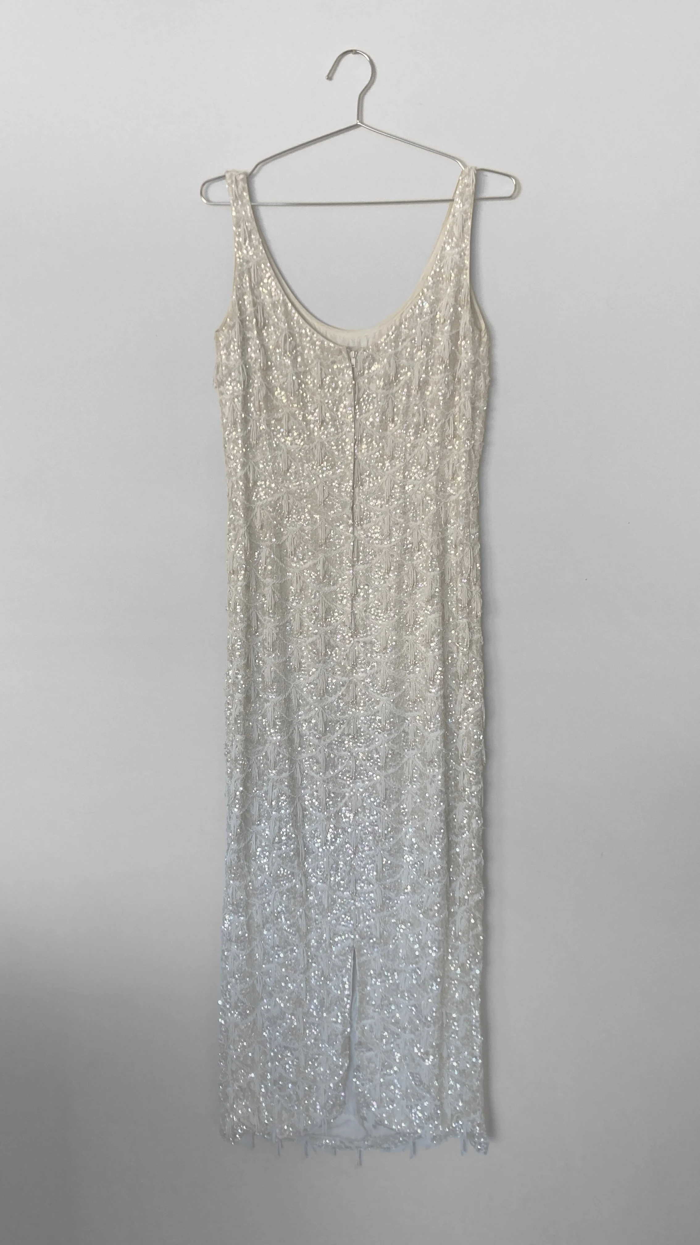 Full length back view of an ivory coloured hand beaded evening gown. It is floor length, sleeveless and has a scoop back, and a centre back metal zip closure.