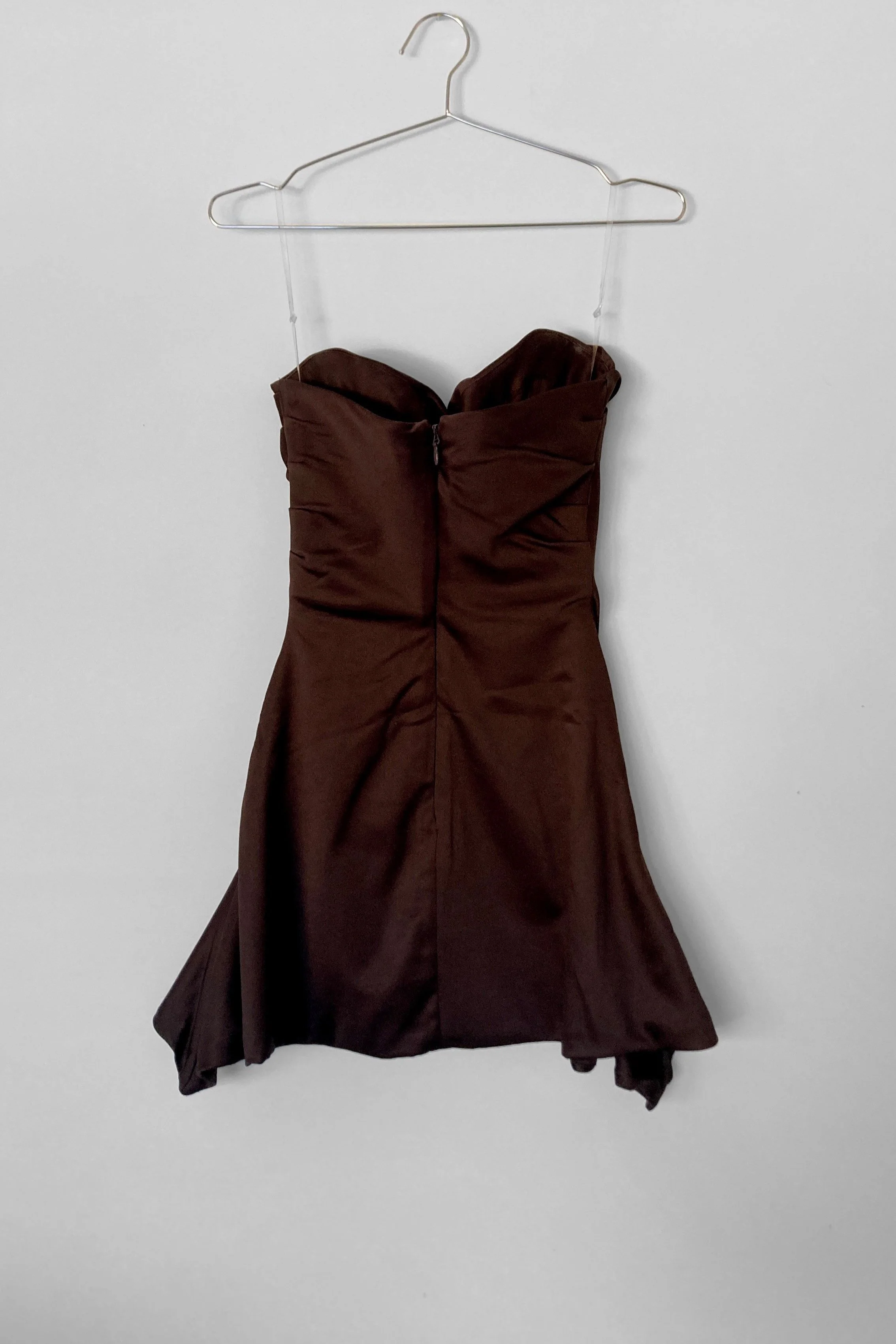 Full view of the back of a strapless chocolate coloured cocktail dress with centre back zip closure. The hem finishes longer at the side seams creating a waterfall effect.