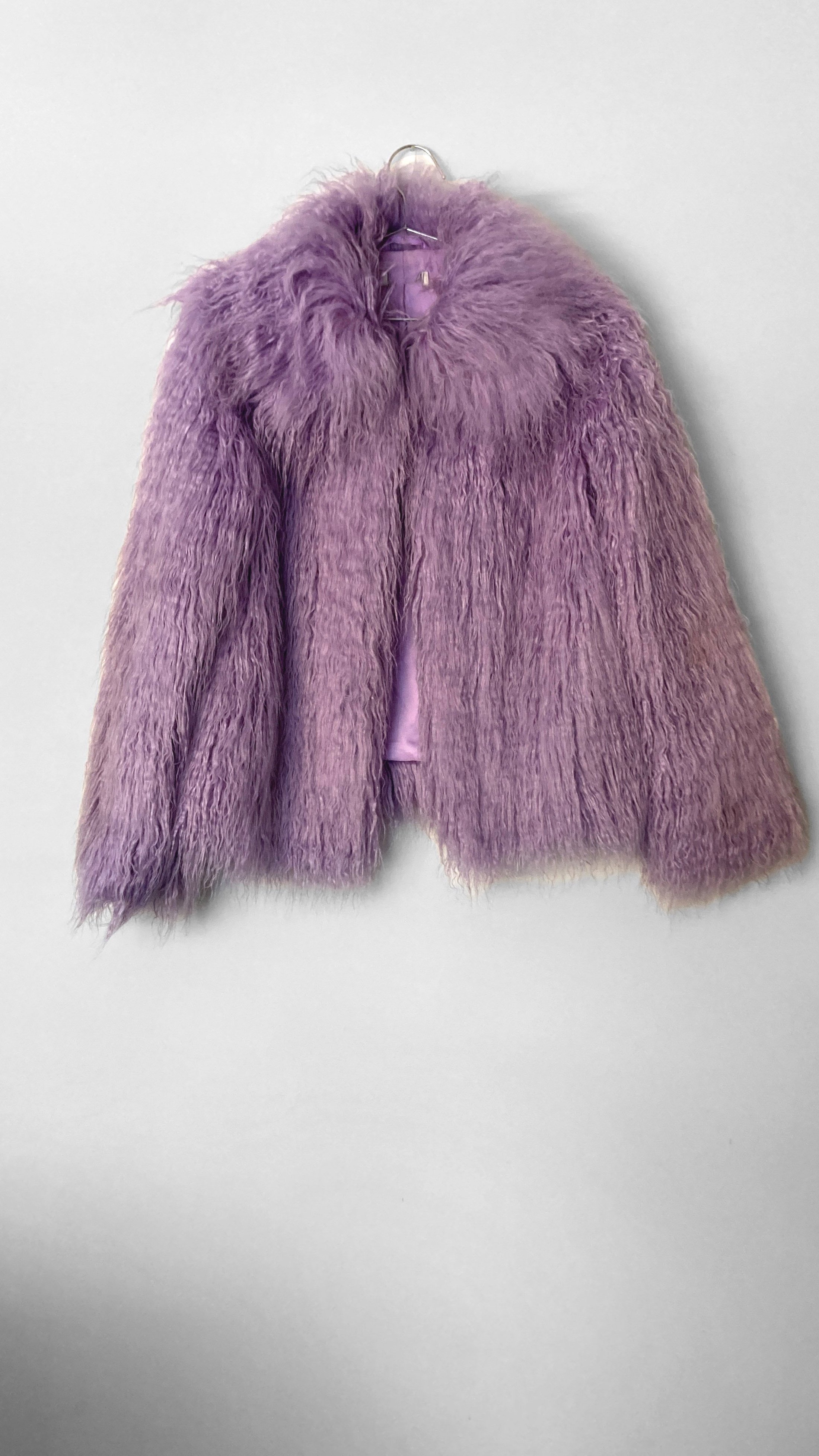 Full view of a lilac-purple hip length faux fur jacket. It has an oversized fur collar, and fastens down the centre front.