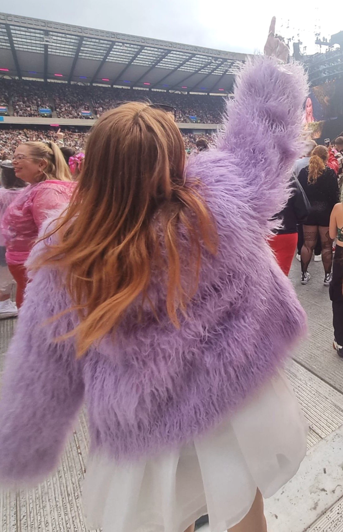 A girl with long ginger hair dances wearing a lilac faux fur jacket over a white puff dress.