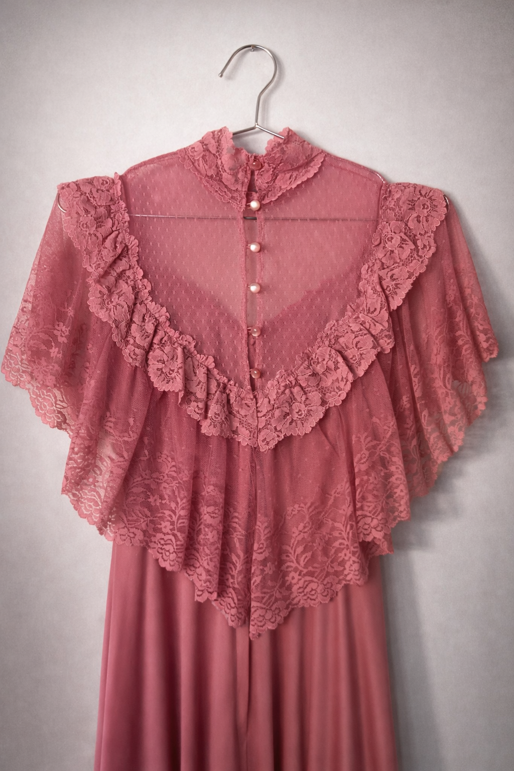 Close up back image of the sheer lace bodice of a vintage rose pink gown. It highlights the lace neck, deep lace frill, and button fastening.