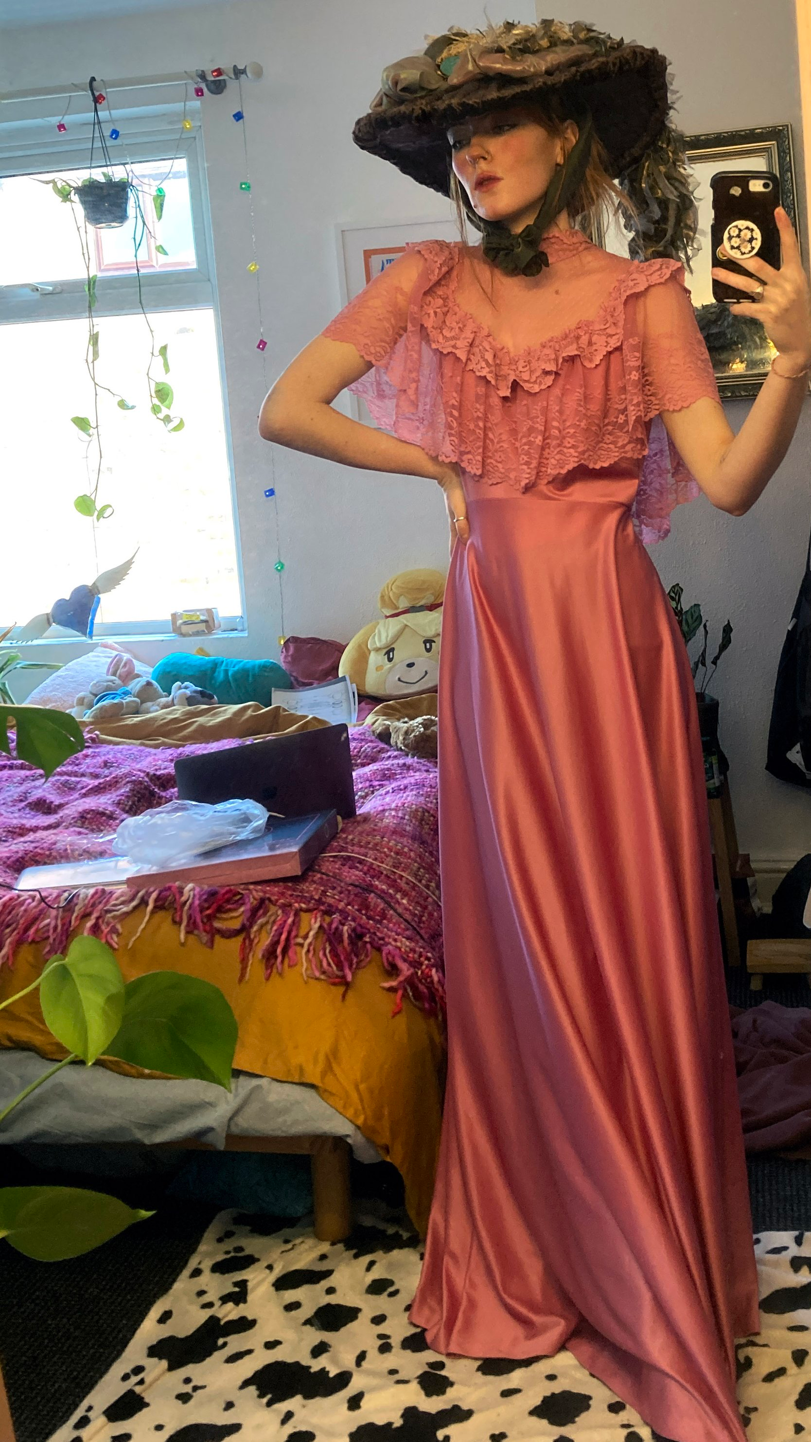A girl poses in the rose pink floor length gown in front of a mirror. She is also wearing an Edwardian style hat, also made by Phoebe Niemira Costume Studio.