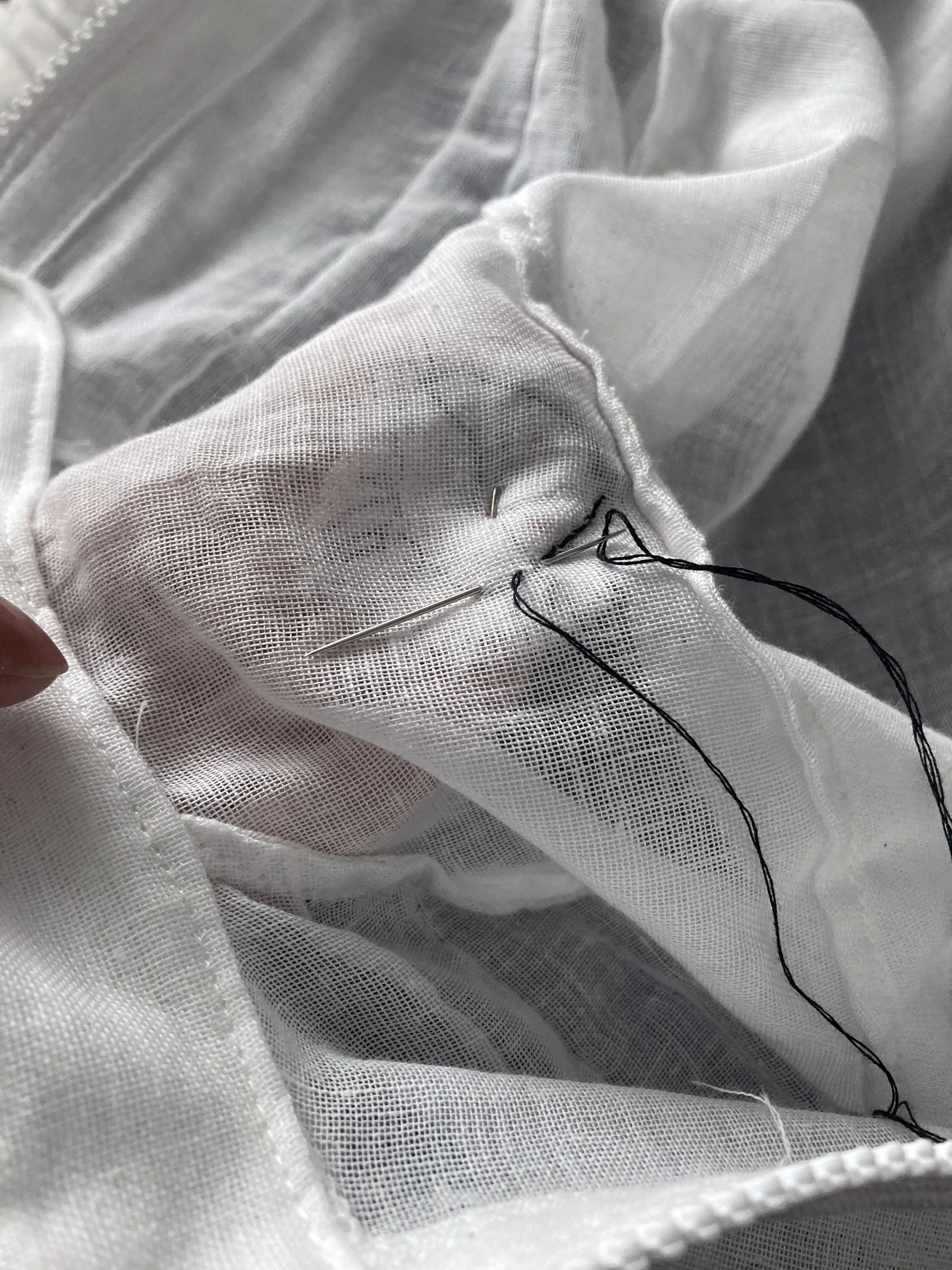 Close up image of a needle and black thread, hand sewing a sacred heart appliqué onto a fine cotton shirt