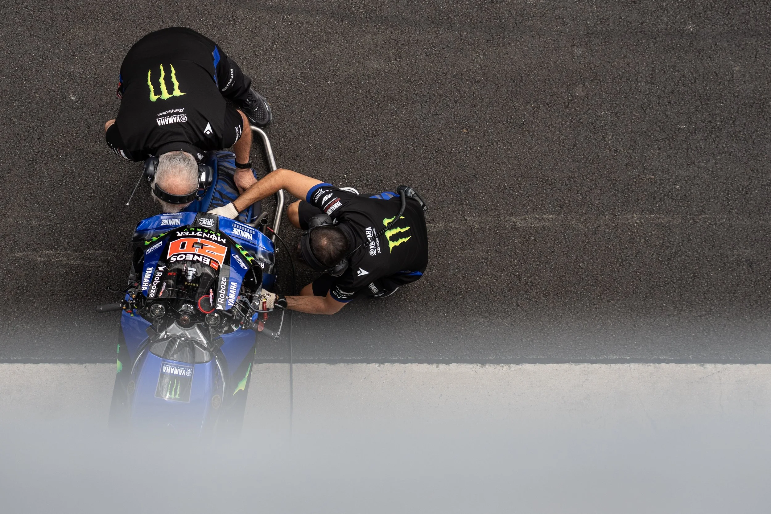 Two motorbike mechanics working on a Yamaha racing motorcycle on a road, viewed from above. MotoGP Brno. Monster Energy.