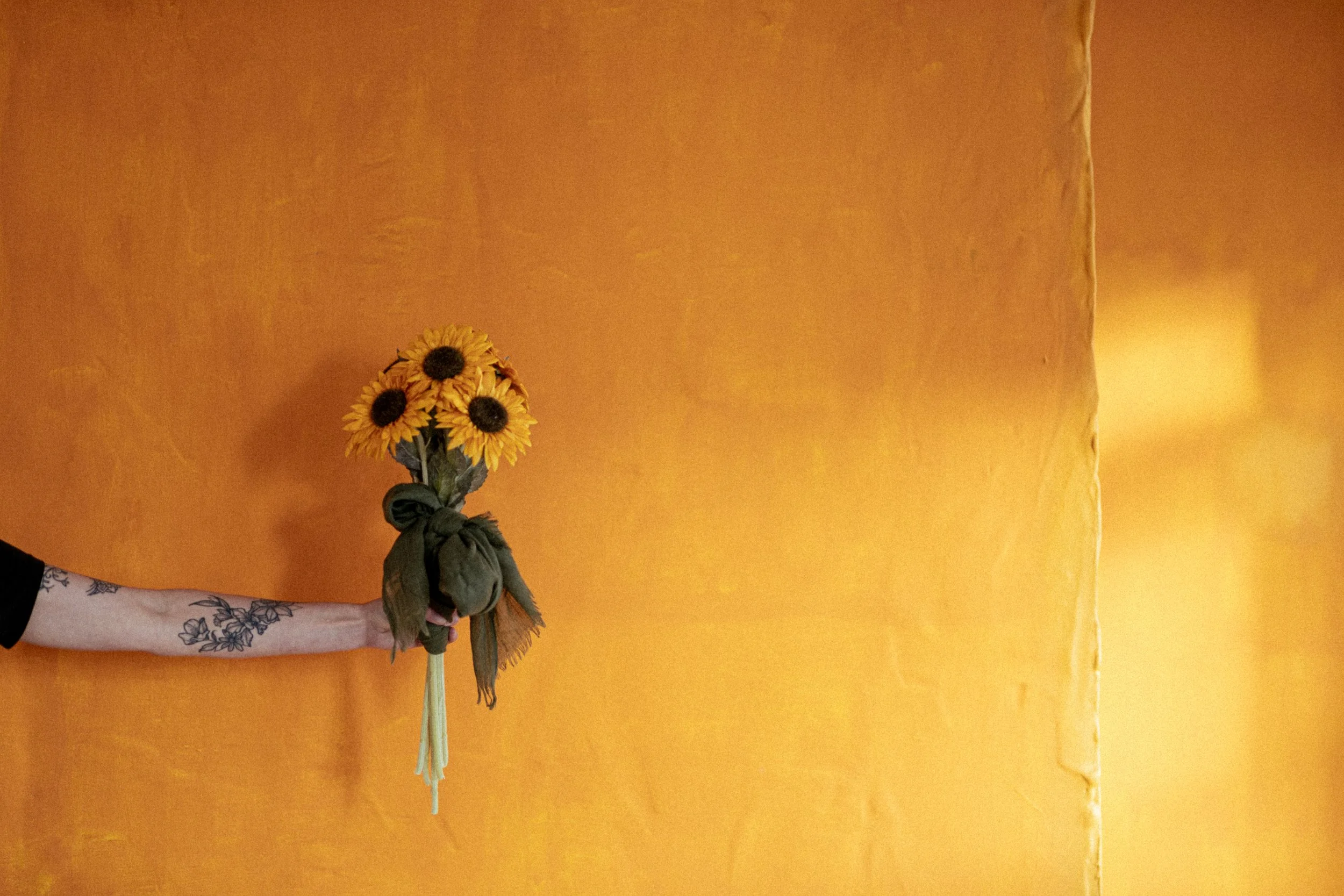 Person holding a bouquet of sunflowers against a yellow wall. Promotional Music Photography.