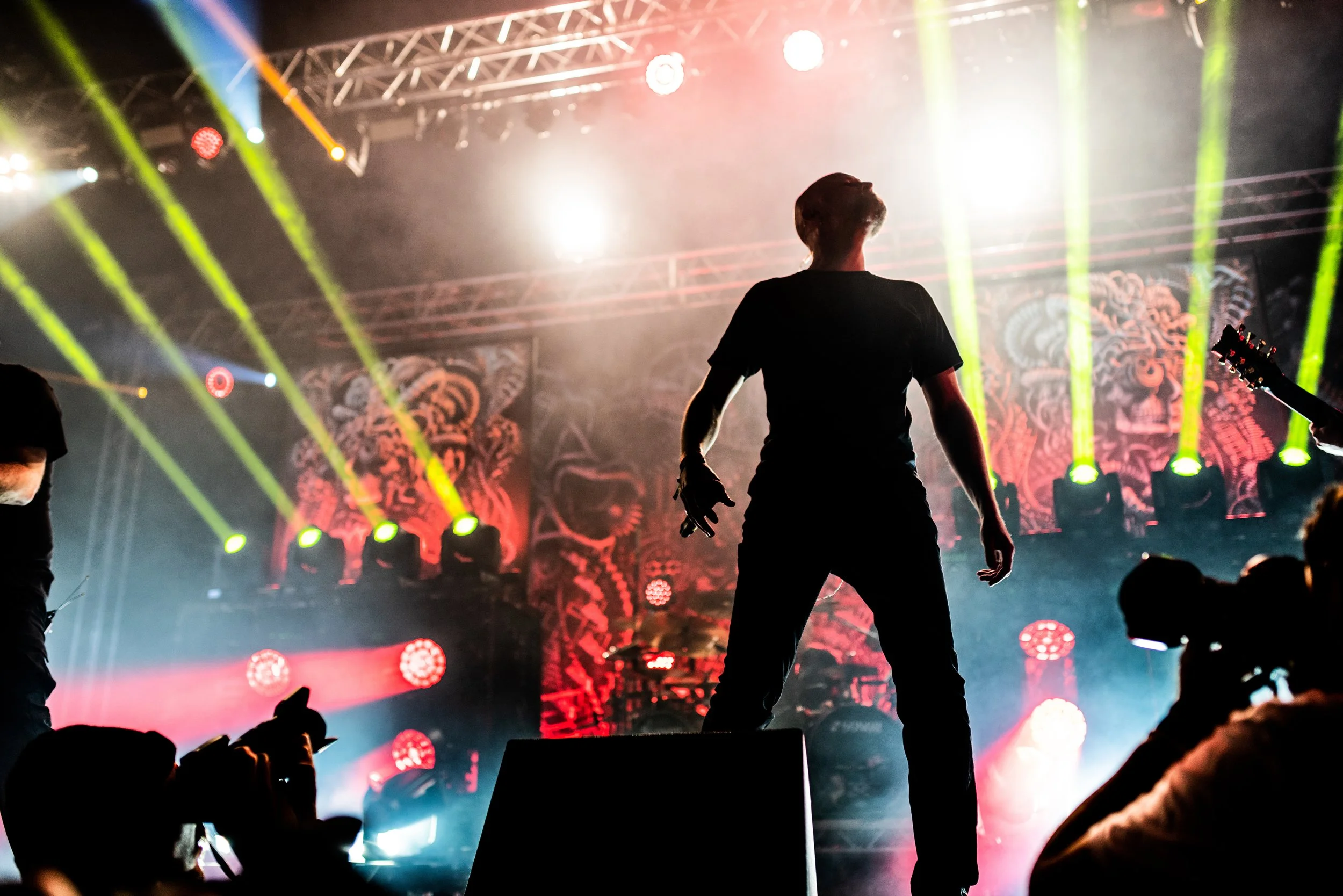 A silhouette of a performer standing on stage in front of vibrant yellow and red stage lights and a colorful backdrop at a concert or live music event. Meshuggah band and ArcTanGent festival.