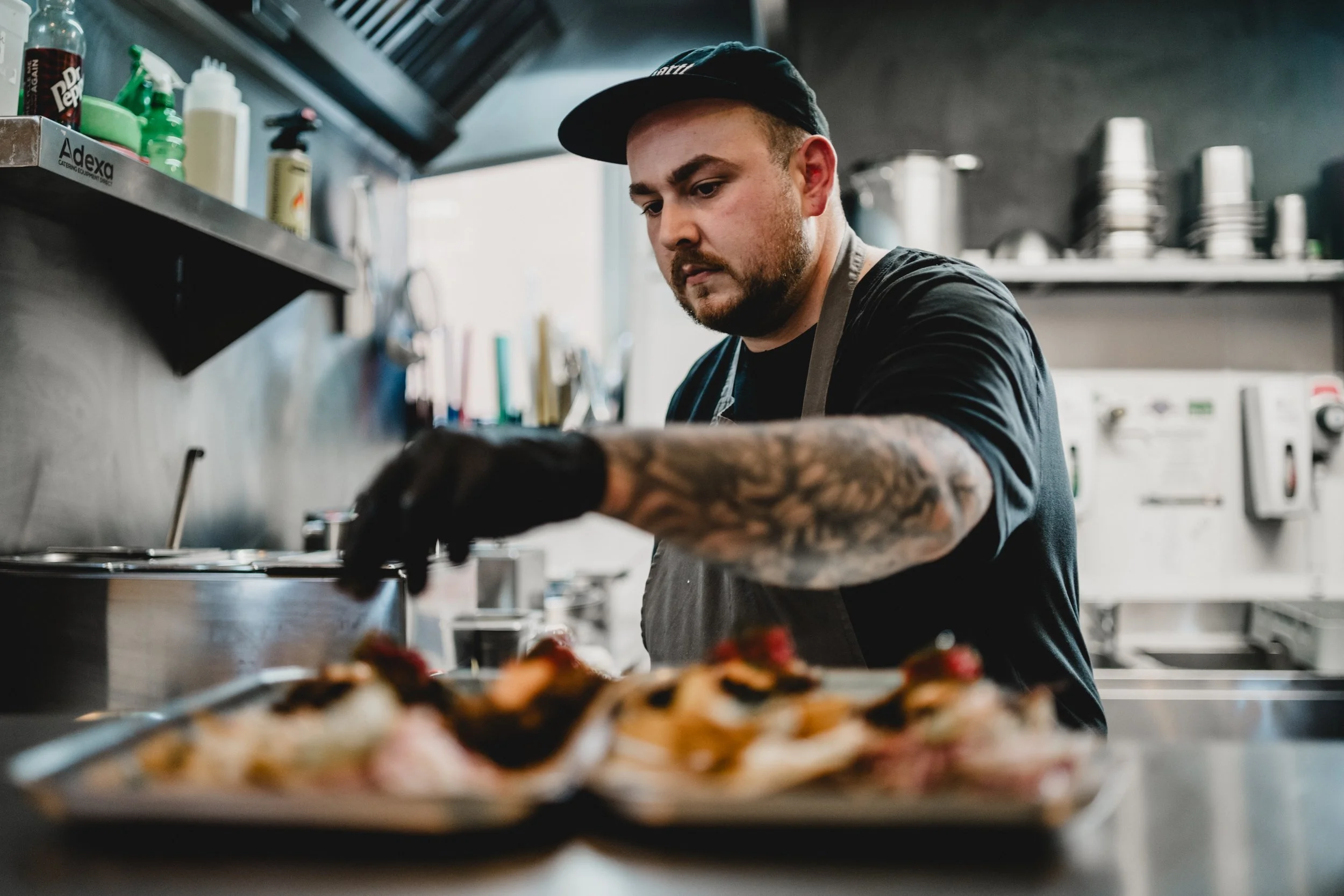A male chef with tattoos on his arm preparing food in a professional kitchen.