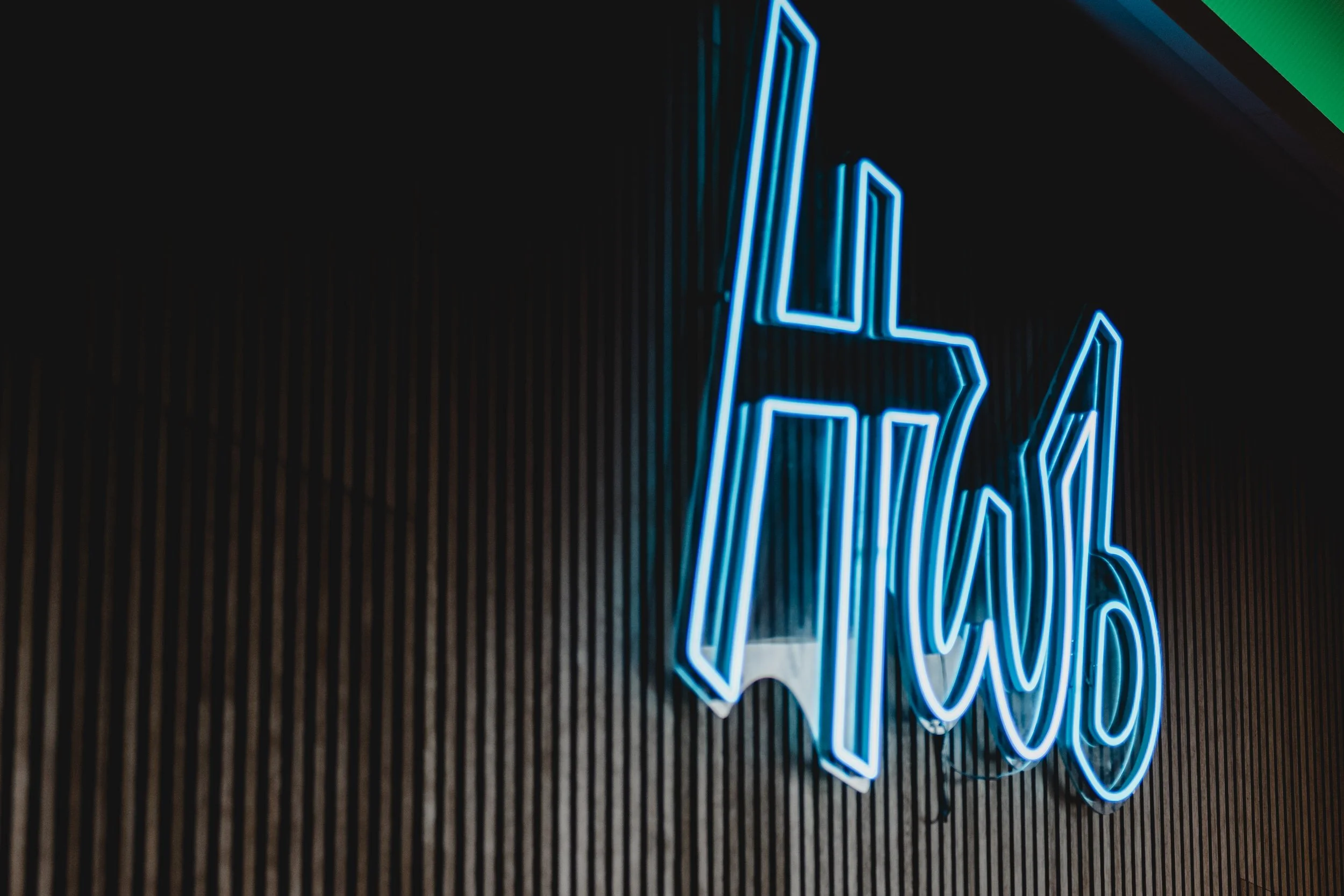 Blue neon sign with the word 'HWB' against a dark wooden wall.