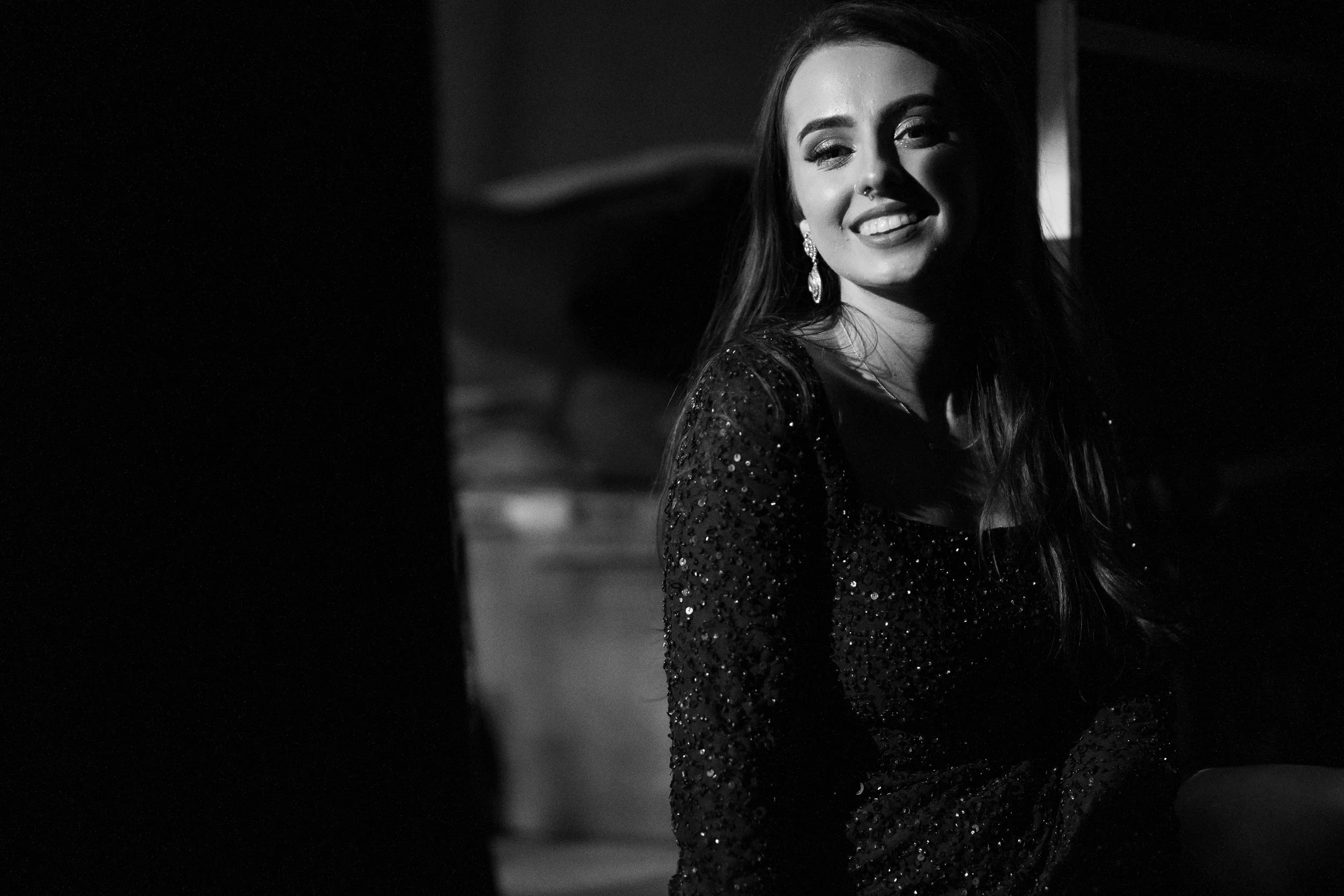 A woman with long hair, earrings, and a sparkling dress smiling in a black-and-white photo. Promotional Music Photography.