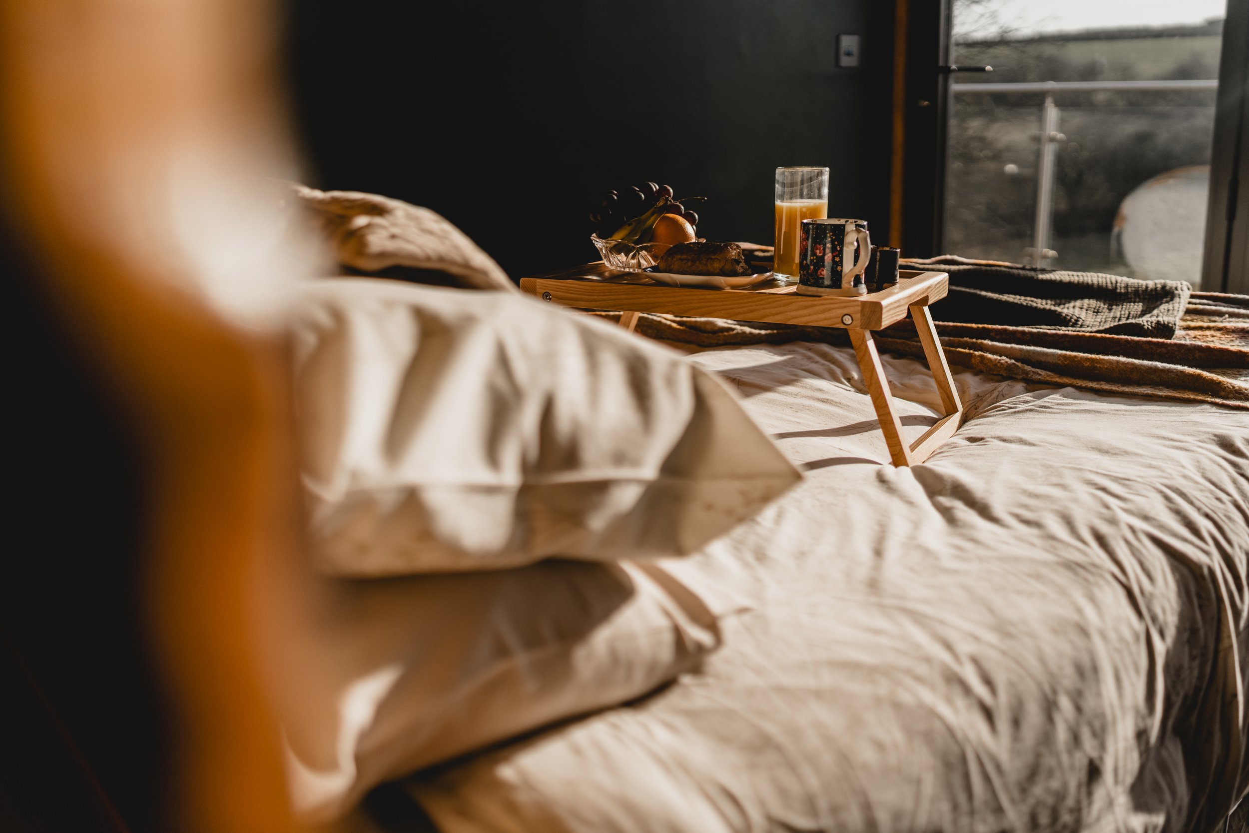 Breakfast tray on bed with juice, coffee, fruit, and pastry in a cozy bedroom.