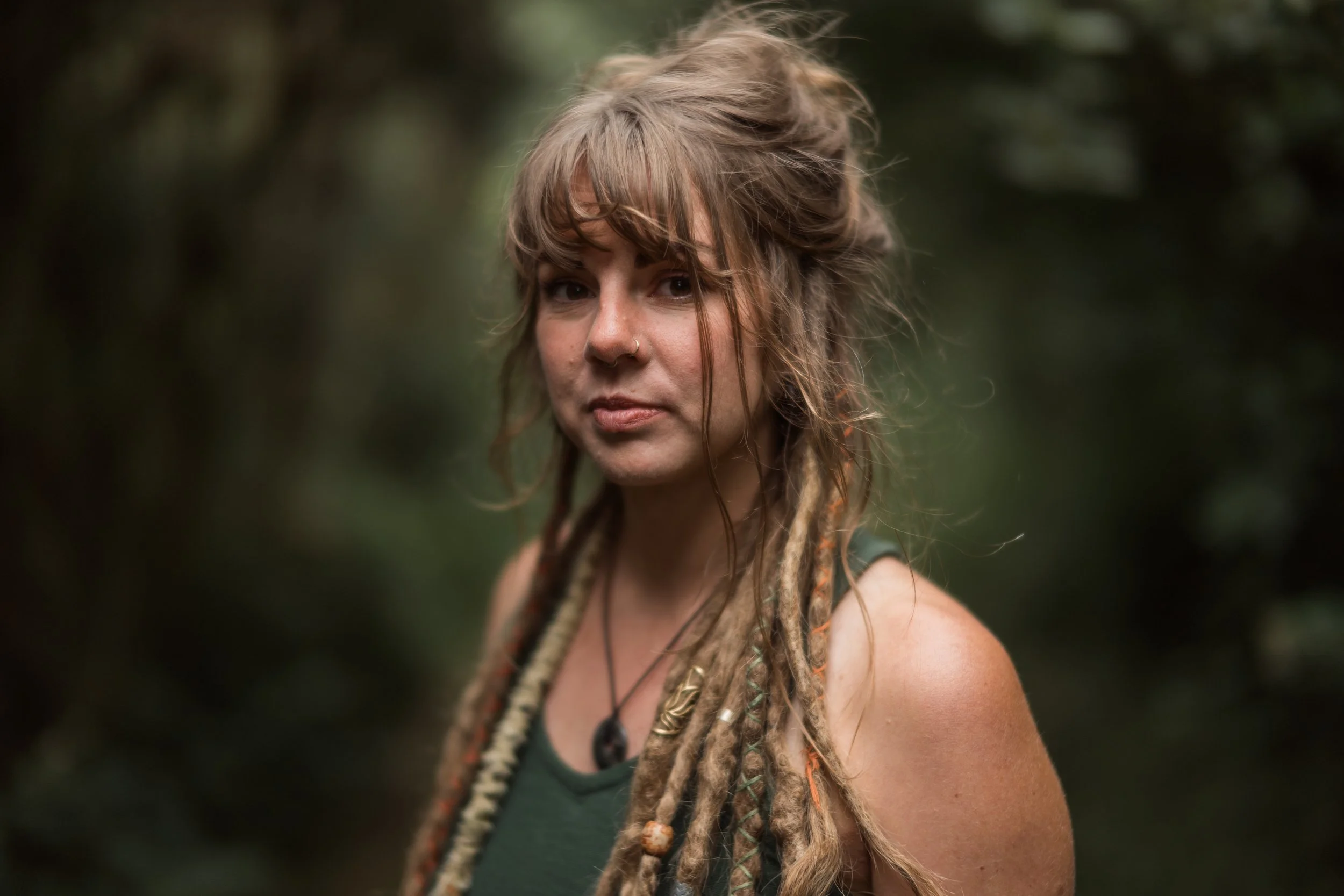 A woman with dreadlocks and a nose ring looking at the camera in a forest setting. Promotional Music Photography.